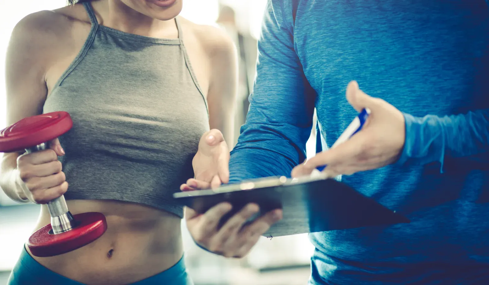 Woman and a fitness instructor talking in a gym while reading notes, much like a package check-in