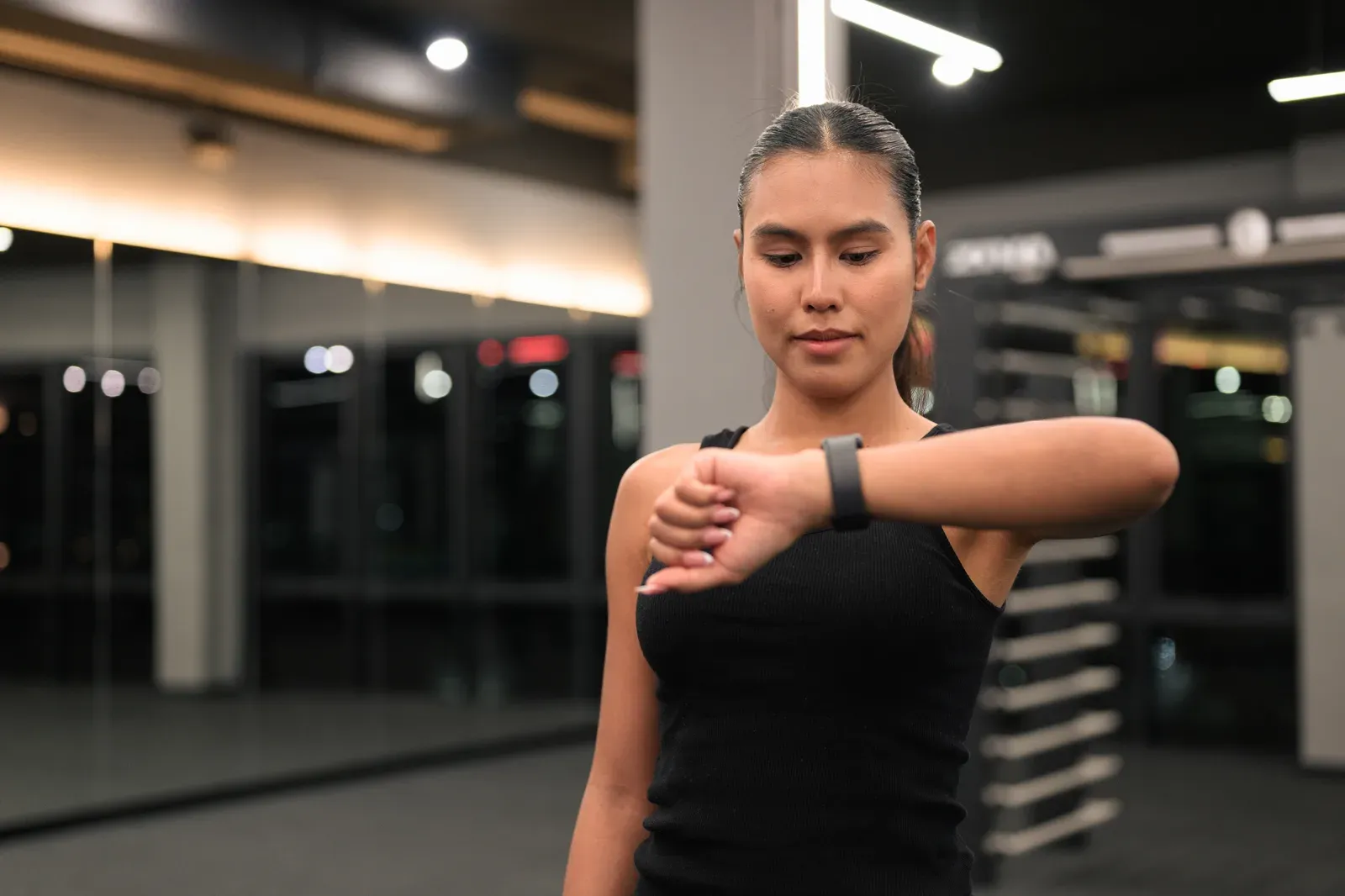 Woman checking her smartwatch during a night workout at the gym, a self-directed option to weigh up