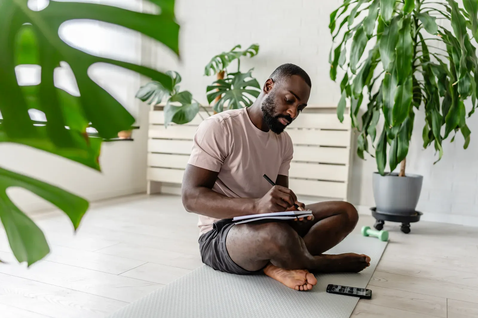 Young man journaling post workout habits on a yoga mat at home
