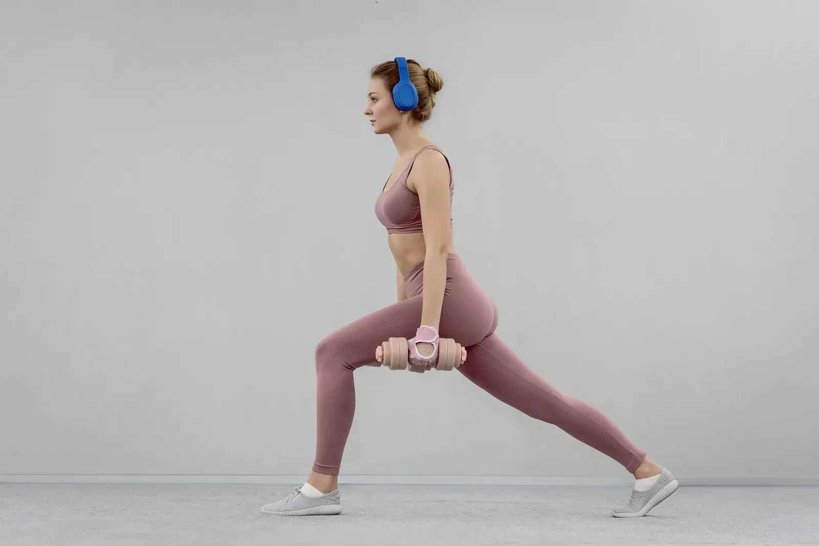Young woman doing a step split stretch with a heavy dumbbell at the gym, a beginner split day in practice