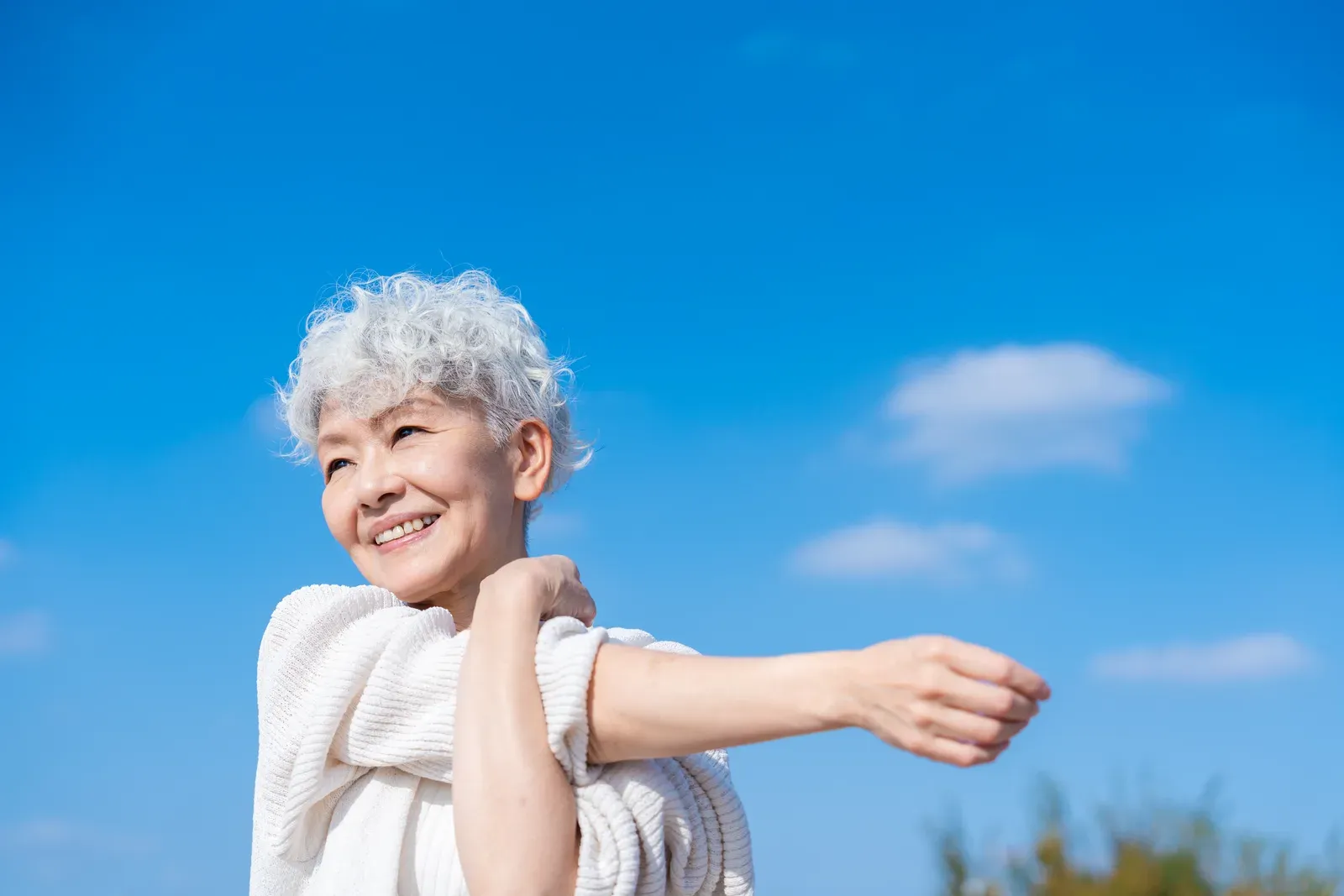 Older woman stretching outdoors under a blue sky, a gentle way to spend an active recovery day