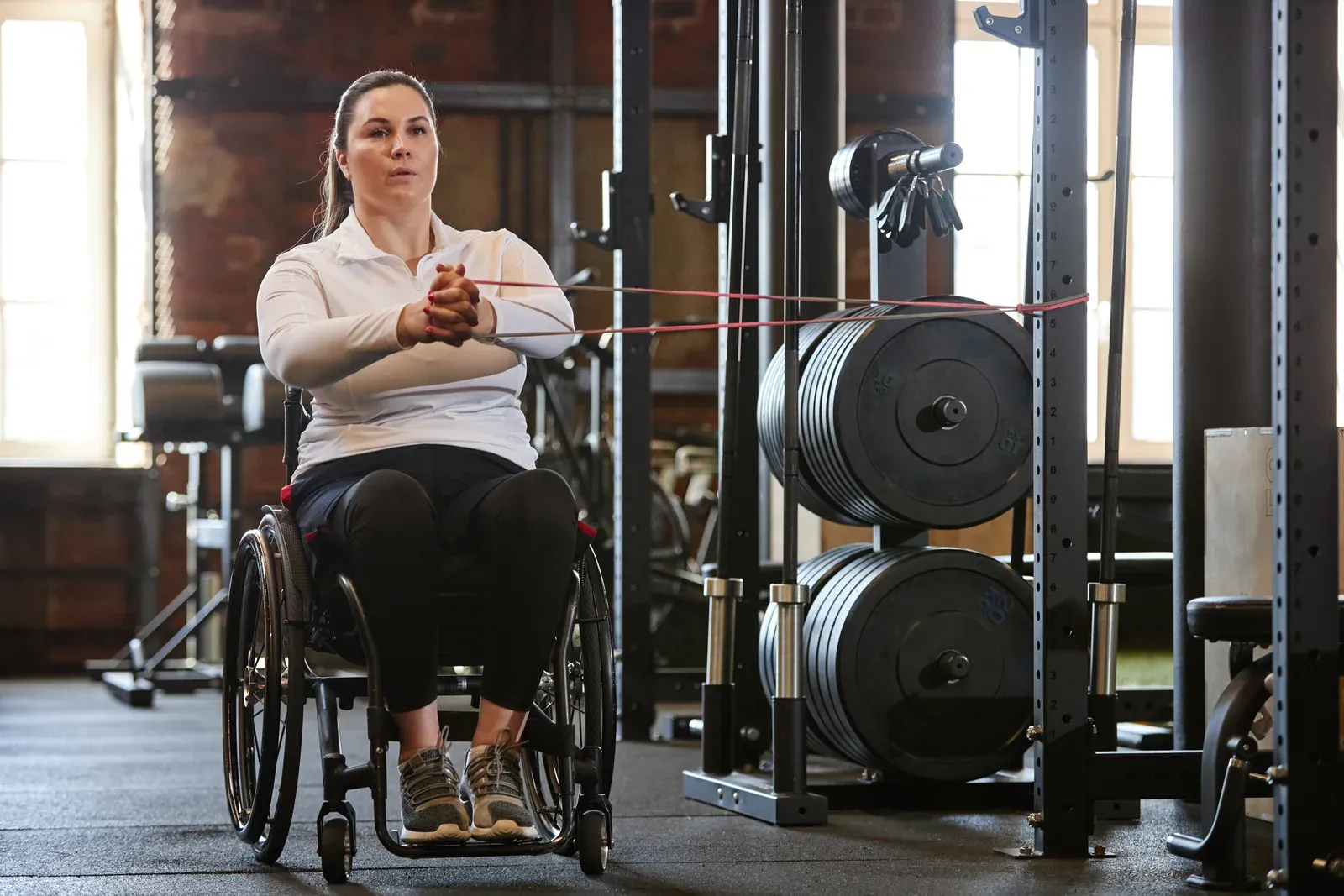 An adaptive athlete training with cable resistance while a coach adjusts the setup