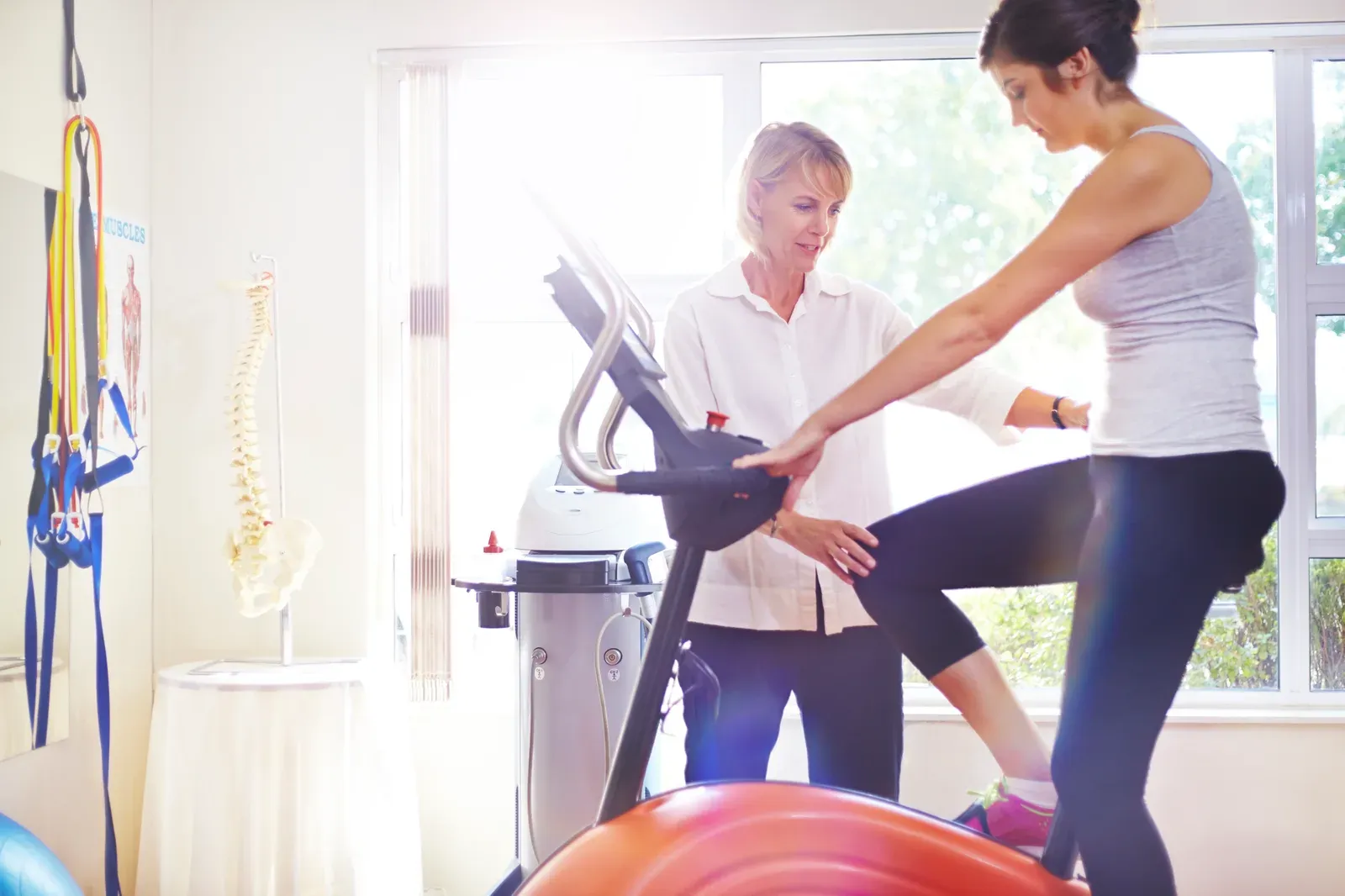 Physical therapist guiding a woman on a stationary bike, light supervised cycling during a return to exercise