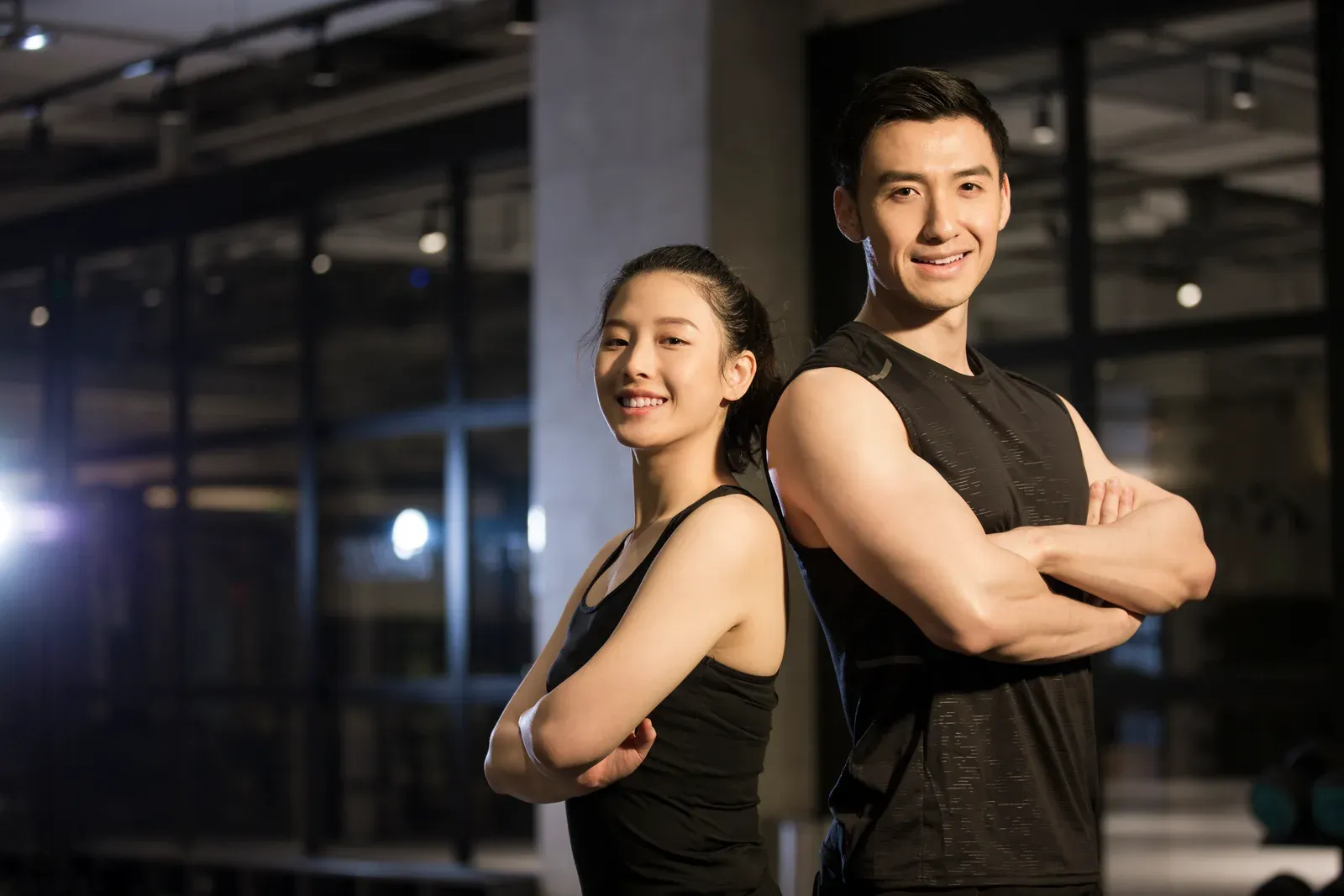 Man and woman standing back to back with arms crossed in the gym, a pairing like supersets that save time