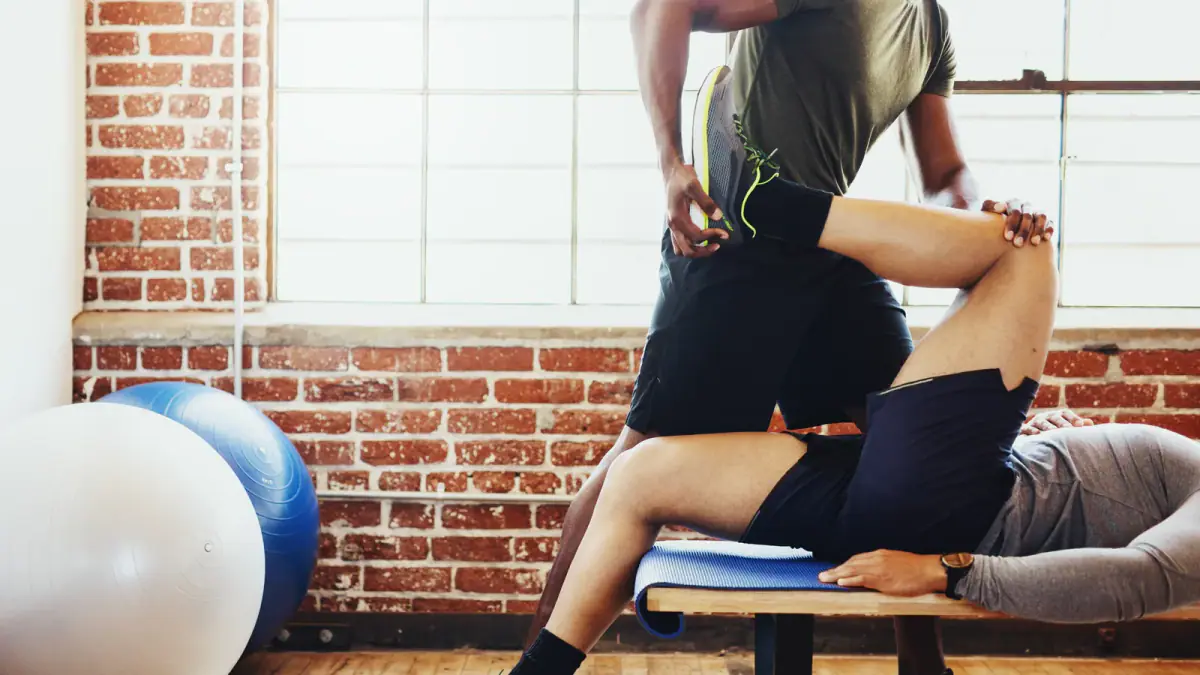 A coach assisting a client through a supported hamstring stretch on a bench