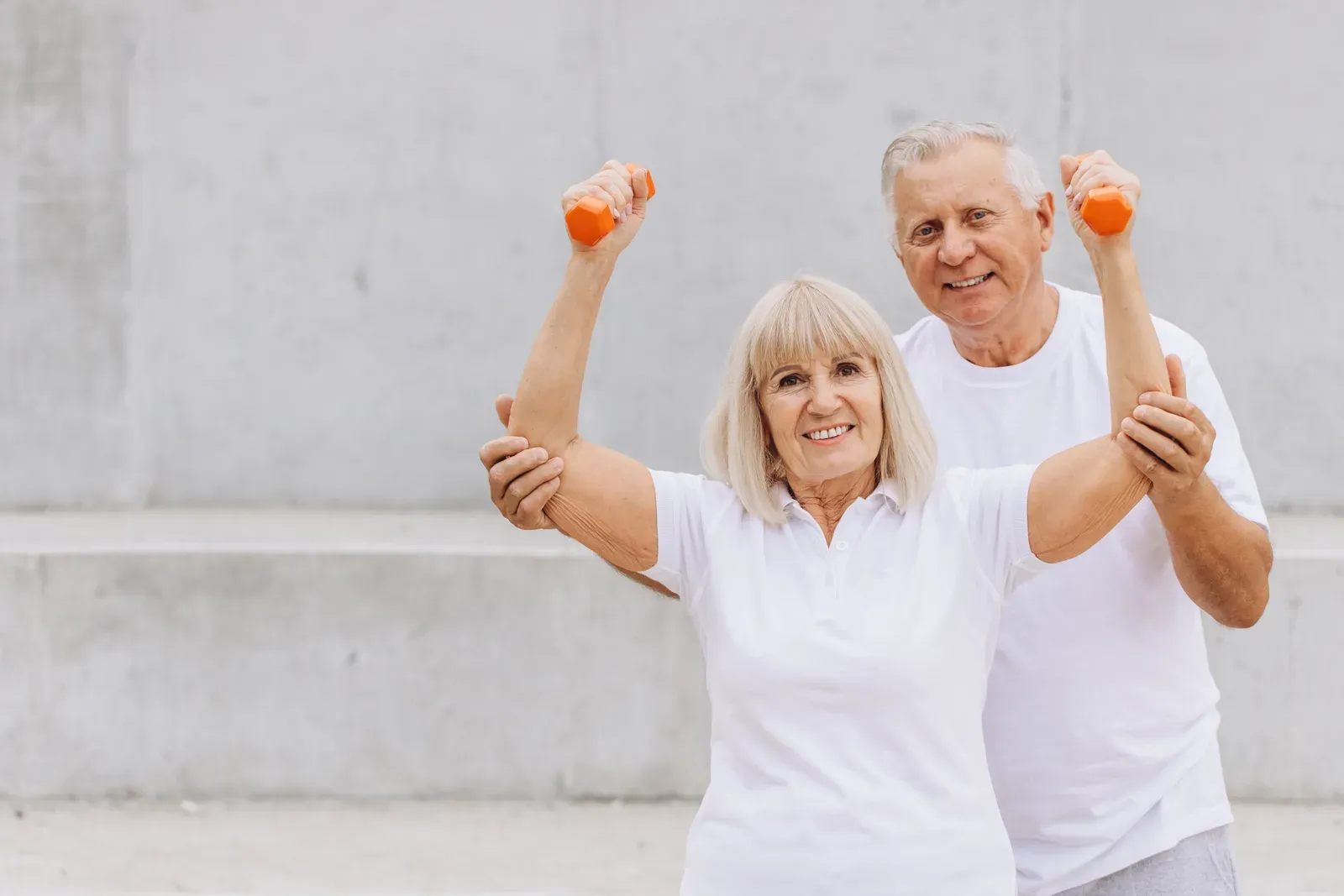 Happy senior couple exercising with dumbbells outdoors in matching white t-shirts, a gentle start at 70