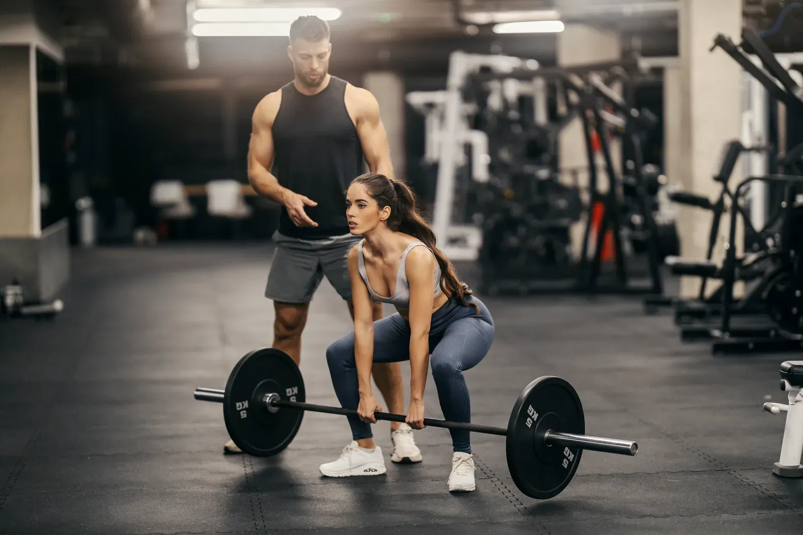 Sportswoman doing deadlifts in a gym while her trainer helps, a compound lift in a fat loss program