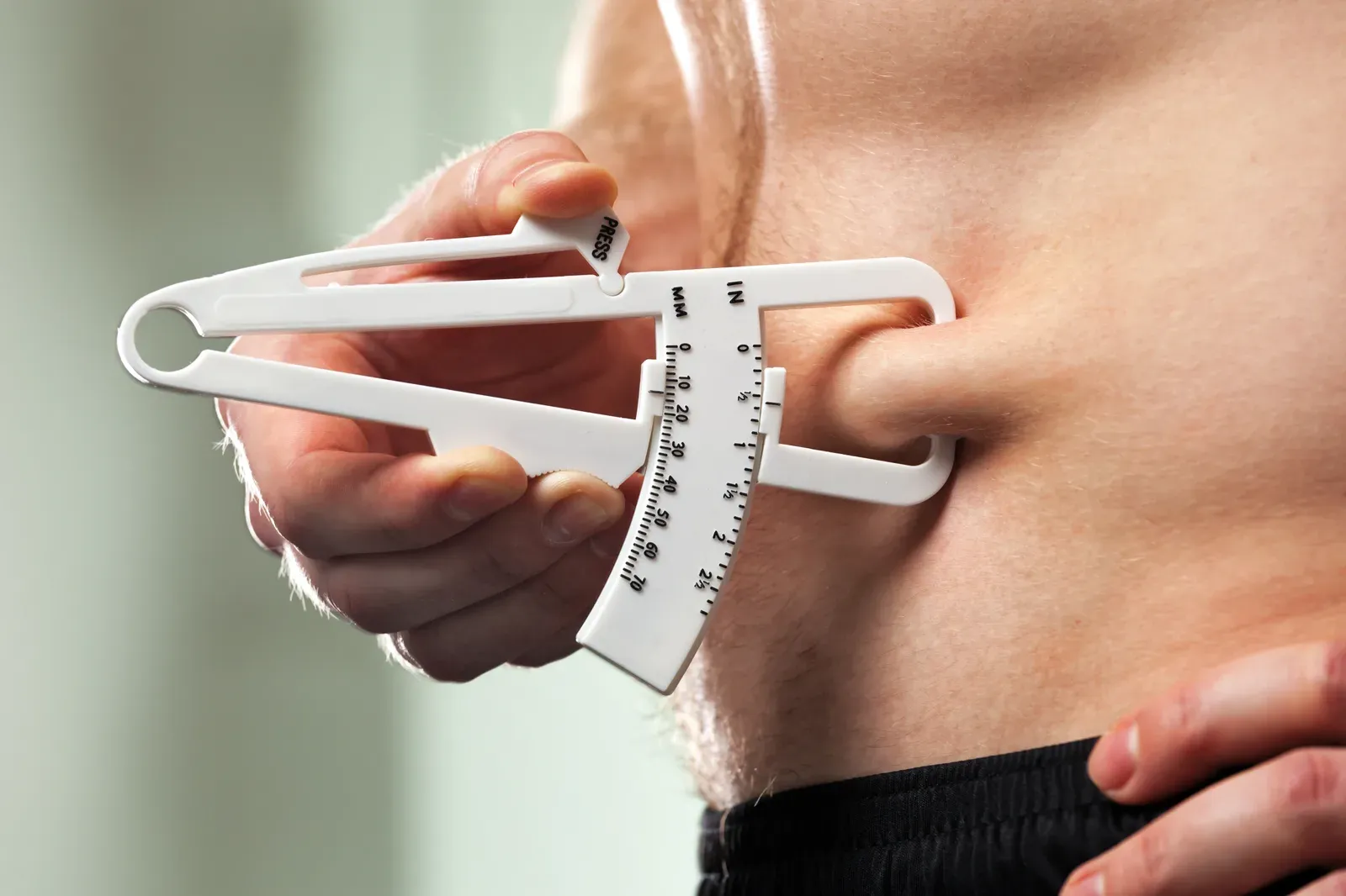 Man measuring his body fat with calipers, one way to estimate fat mass versus fat percentage