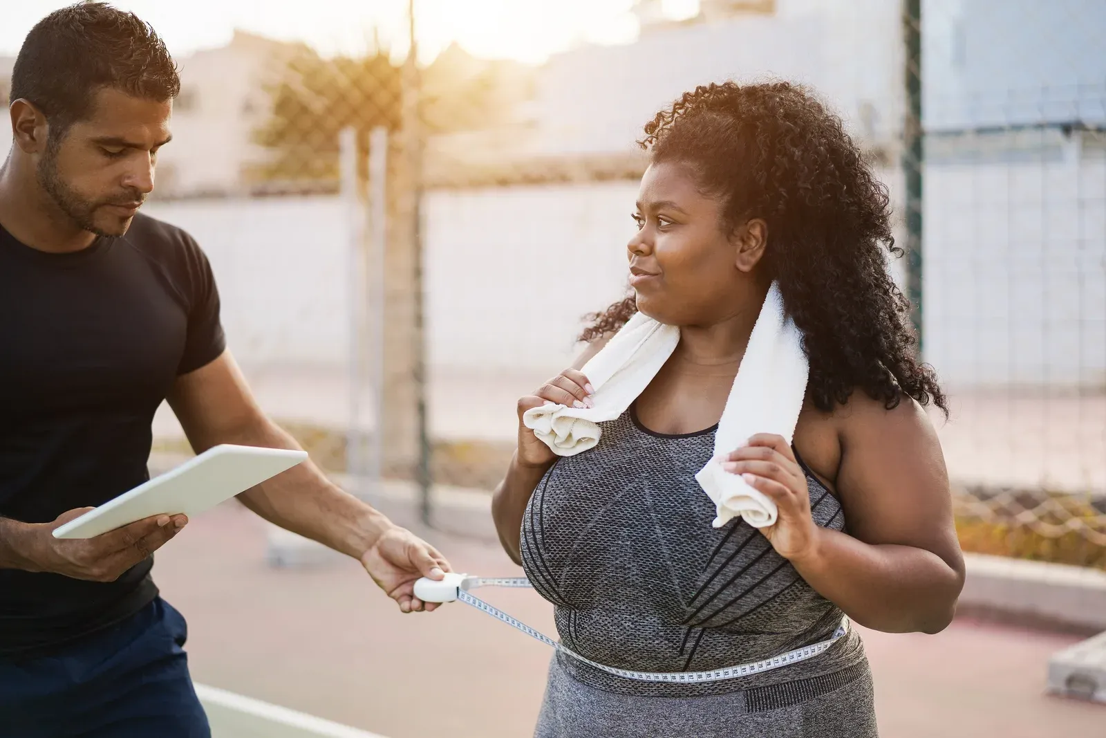 Larger-bodied woman and her personal trainer measuring her waist outdoors, tracking progress toward a goal
