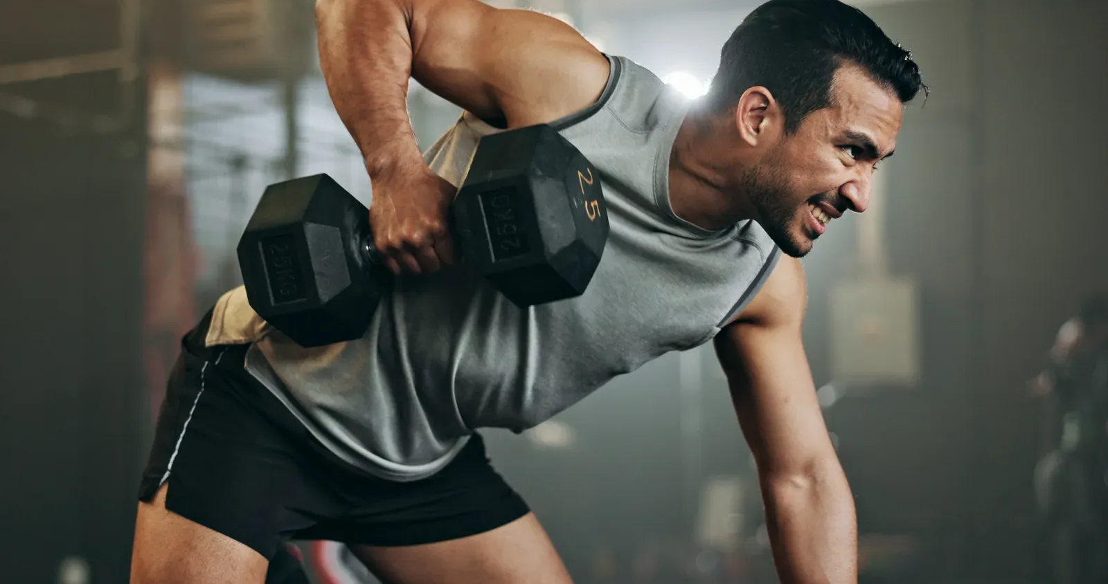 Muscular man performing a strict dumbbell curl in front of a gym mirror