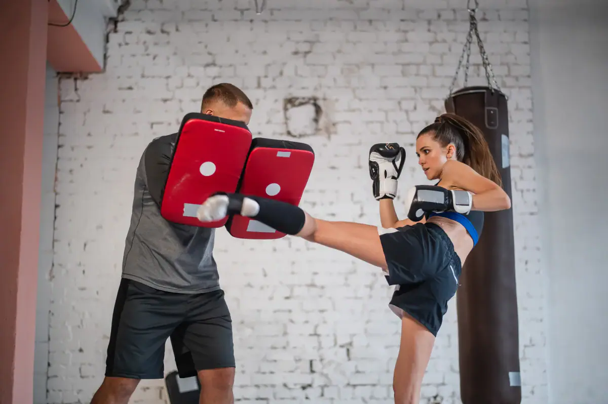 Woman driving a punch into a coach's striking pads during a private kickboxing workout