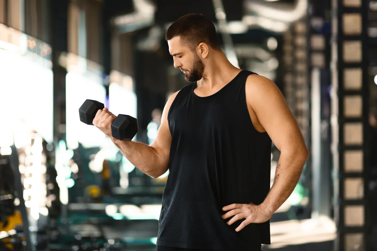 Muscular man performing dumbbell curls at the gym during the day, an arm focus common in a bro split