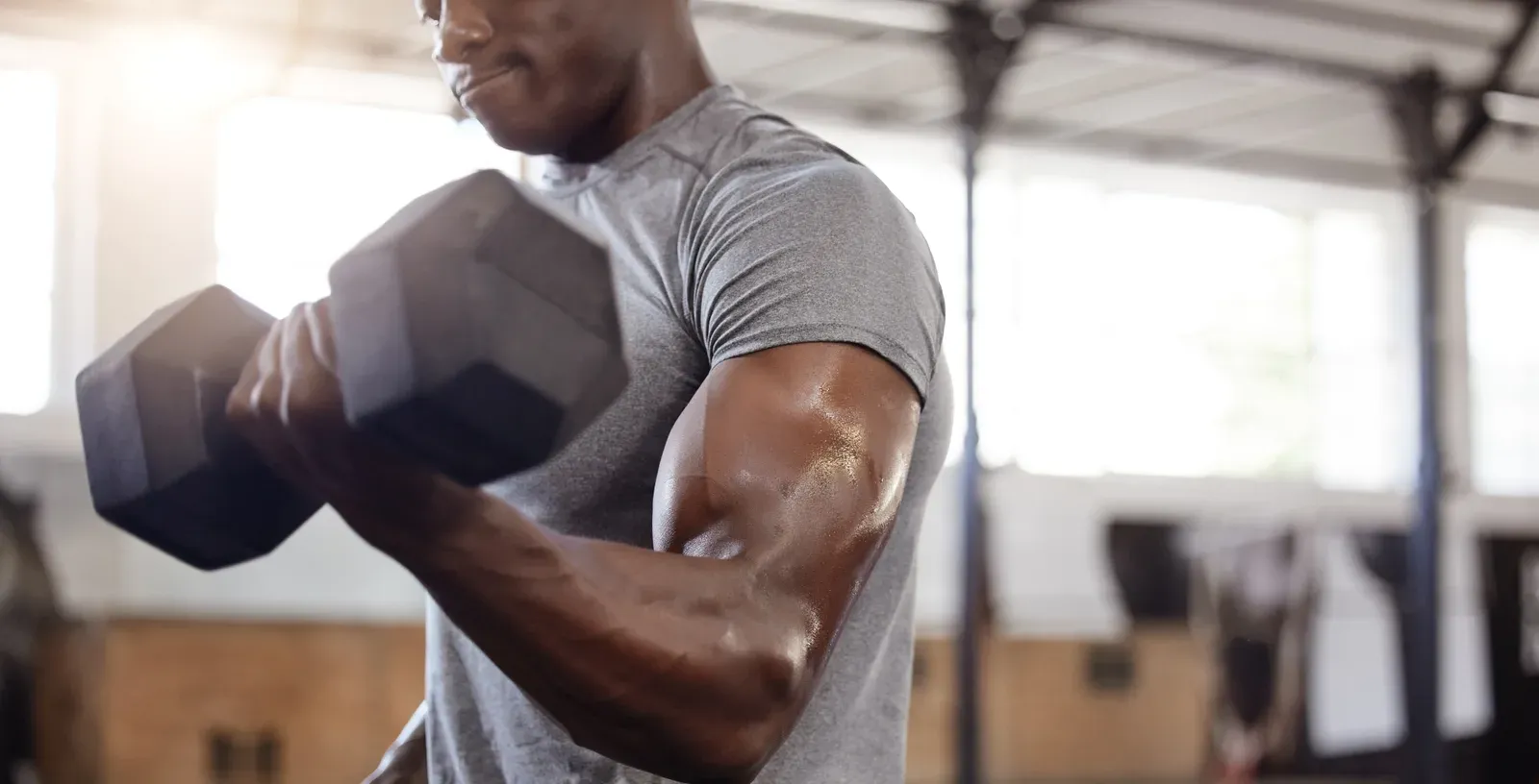 Athlete lifting a dumbbell in a bicep curl in the gym, an arm exercise to adapt after 40 to spare the elbows