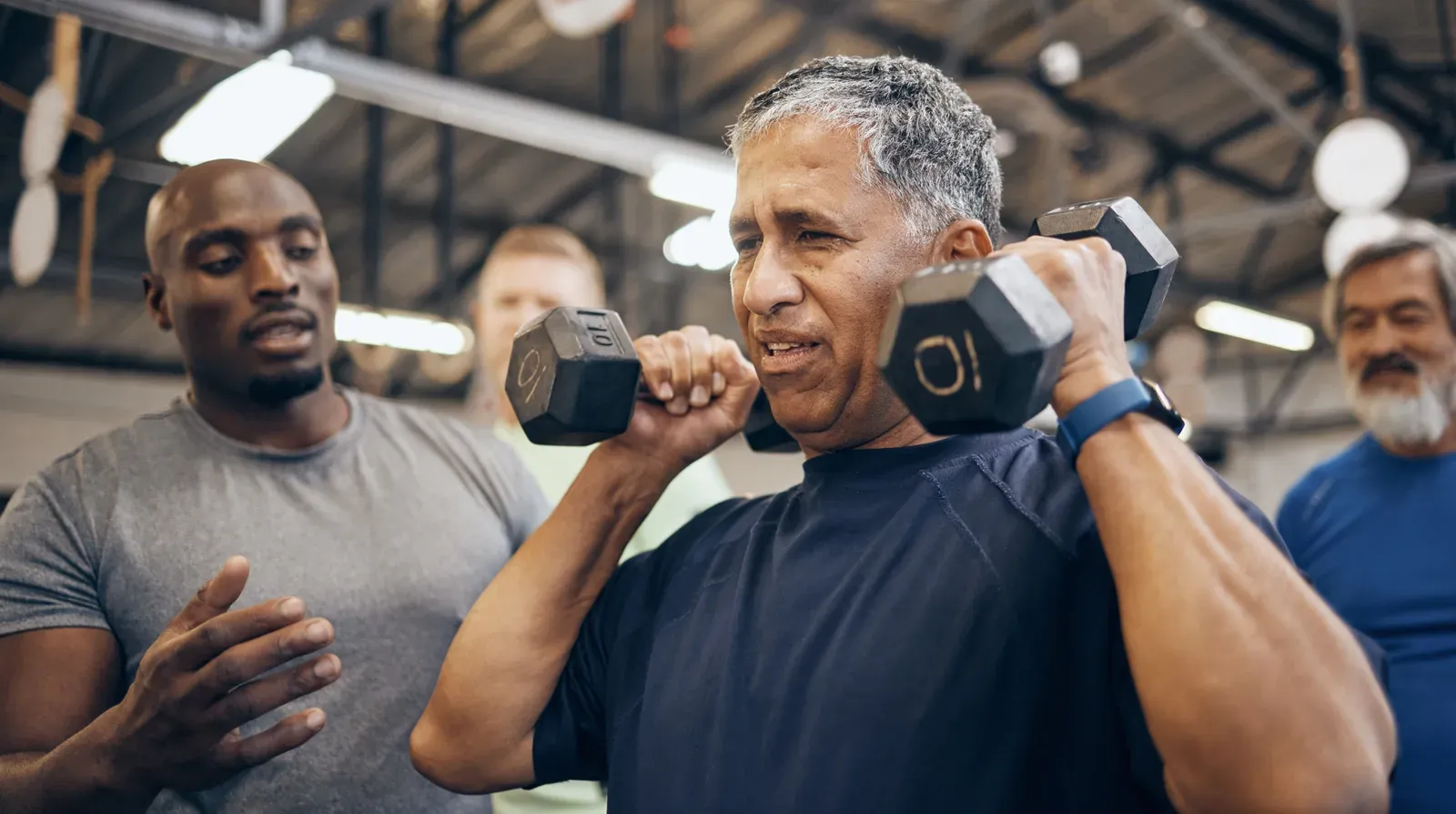 Older man lifting a dumbbell with help from a coach, strength work for building muscle after 60