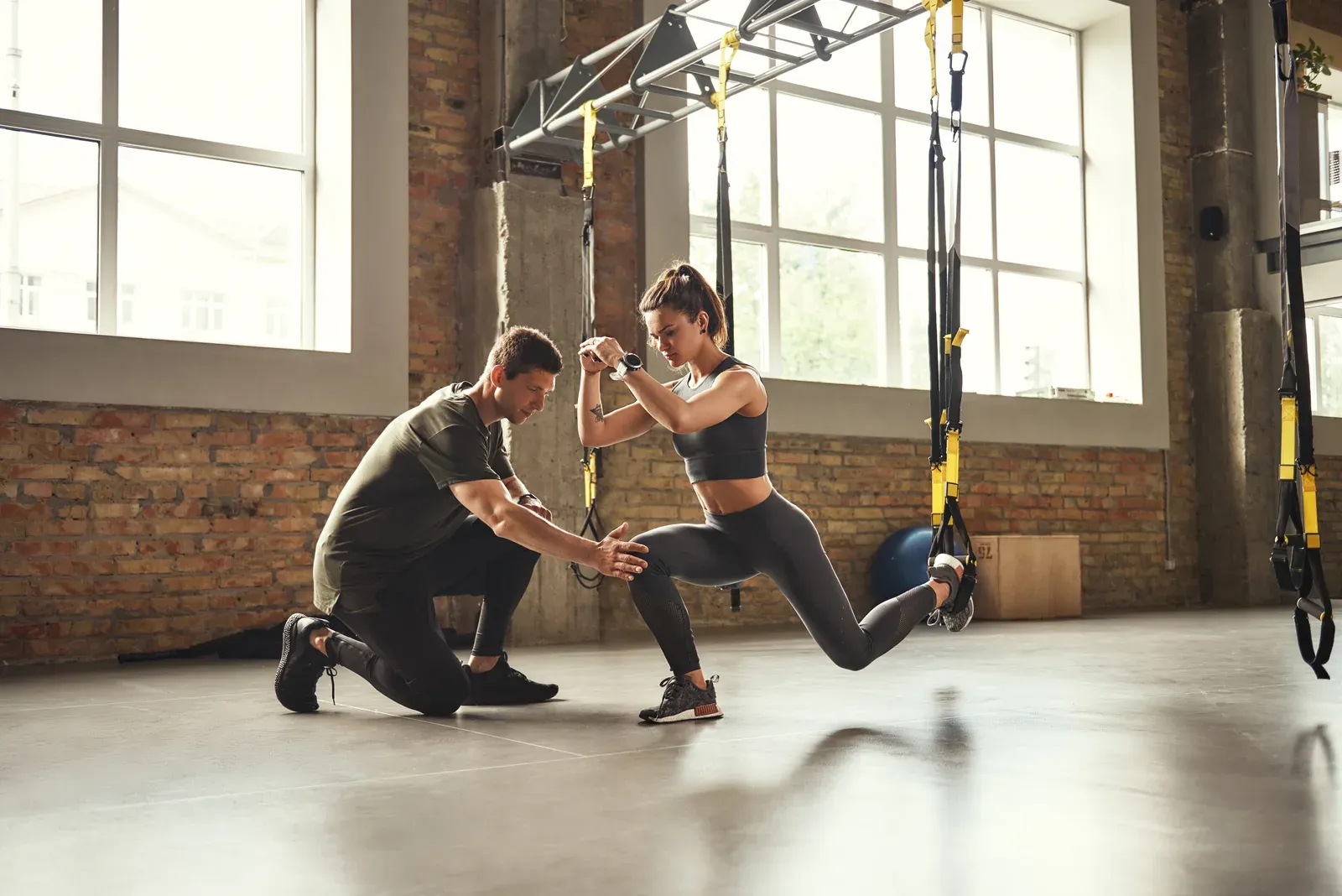 Personal trainer showing a slim woman how to squat, coached lifting for someone trying to bulk up