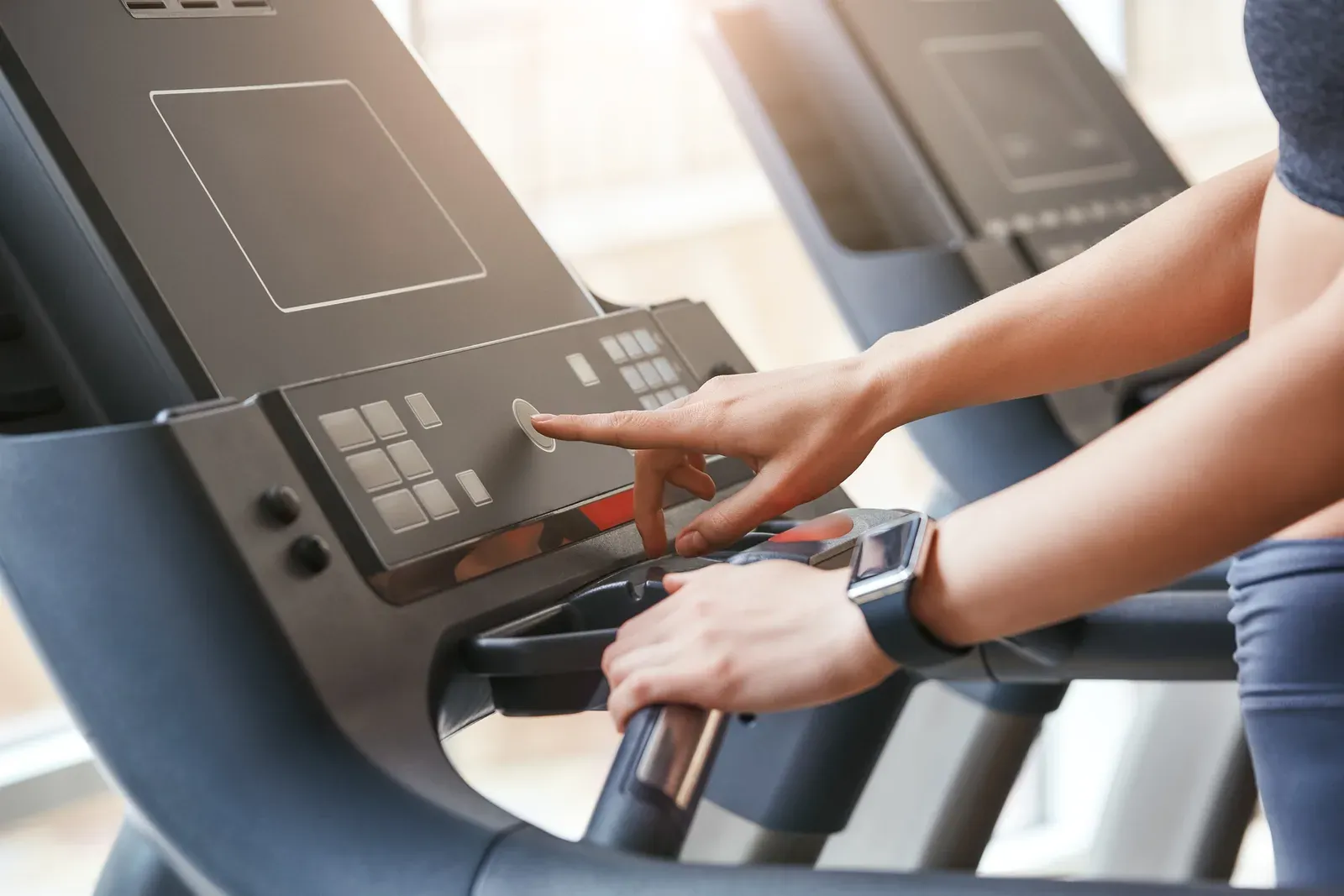 Woman in sportswear pressing the start button on a treadmill at the gym, starting a weekly cardio routine