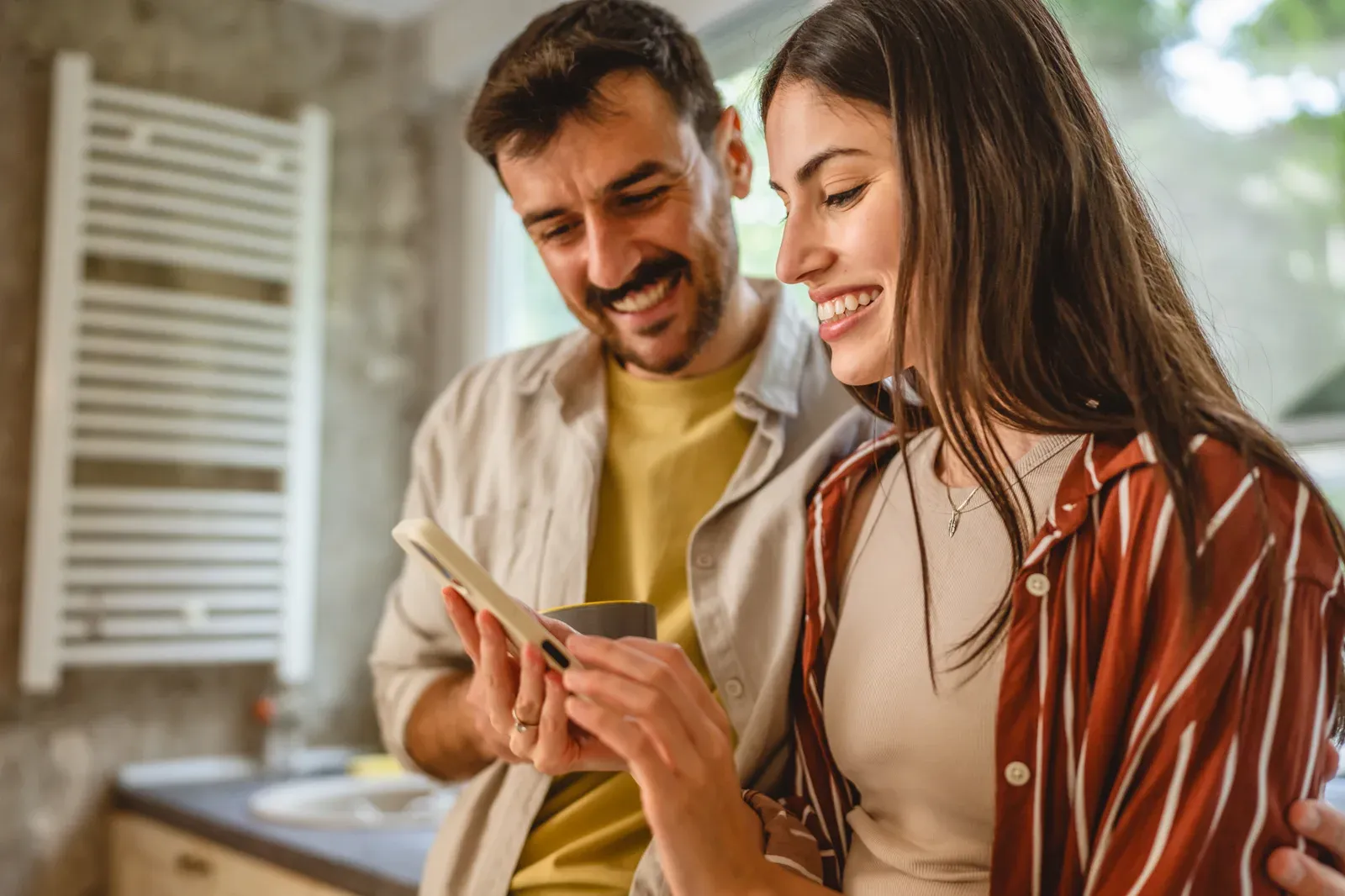 Happy couple in the kitchen using a mobile phone together, comparing schedules that do not line up
