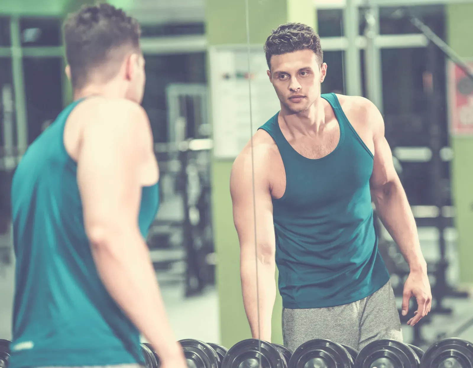 Sportsman standing in front of the mirror in the gym, a moment to weigh whether to cut or bulk first
