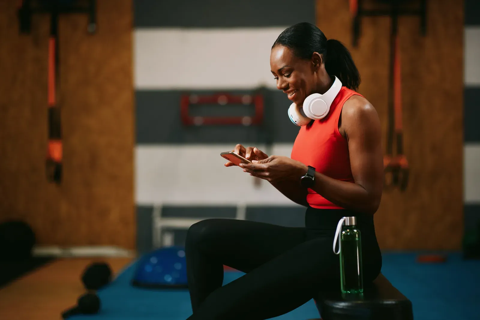 Smiling woman using a smartphone app in the gym after a workout, logging what she did