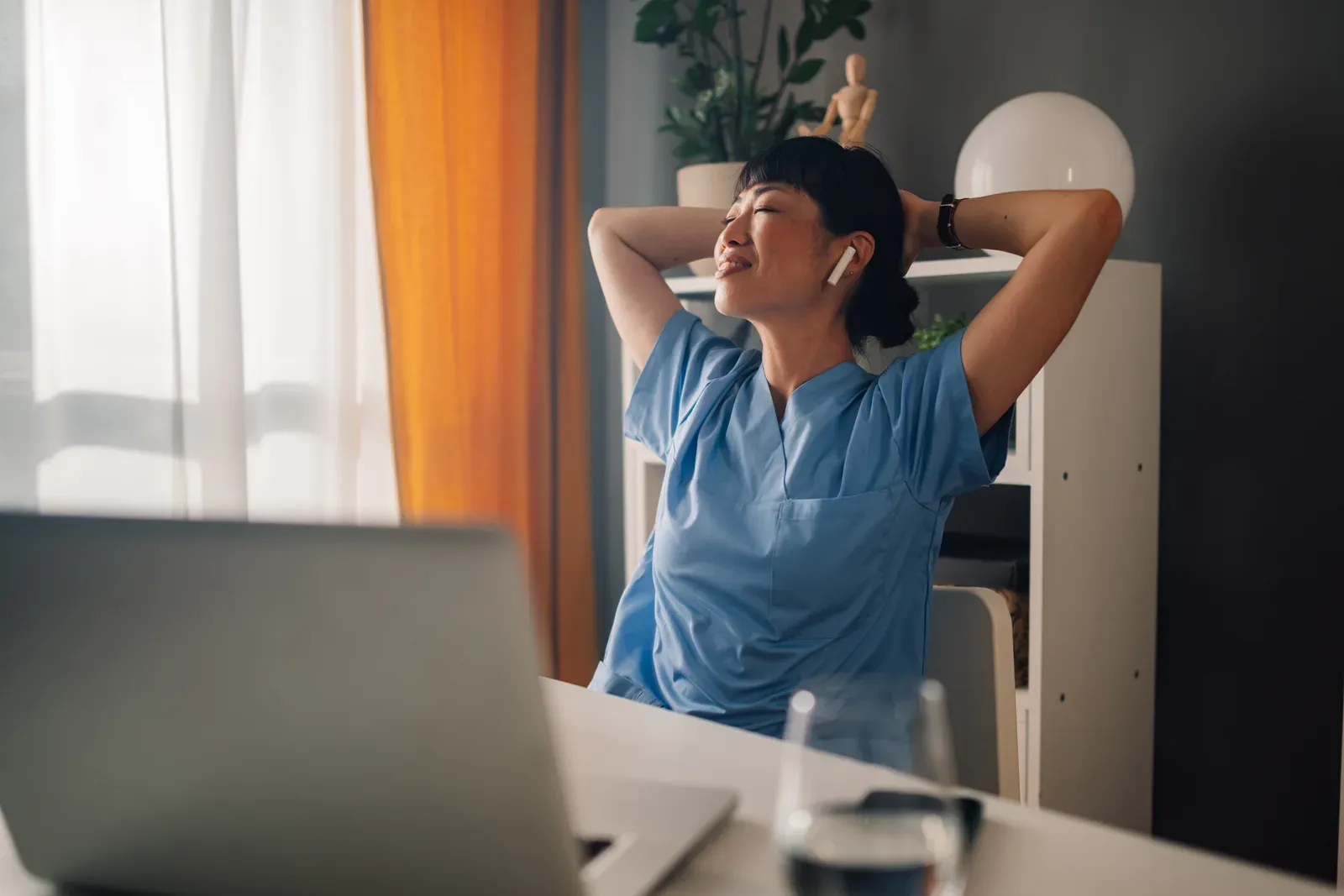 Woman nurse in blue scrubs stretching while seated at a desk, a quick reset on a demanding work schedule