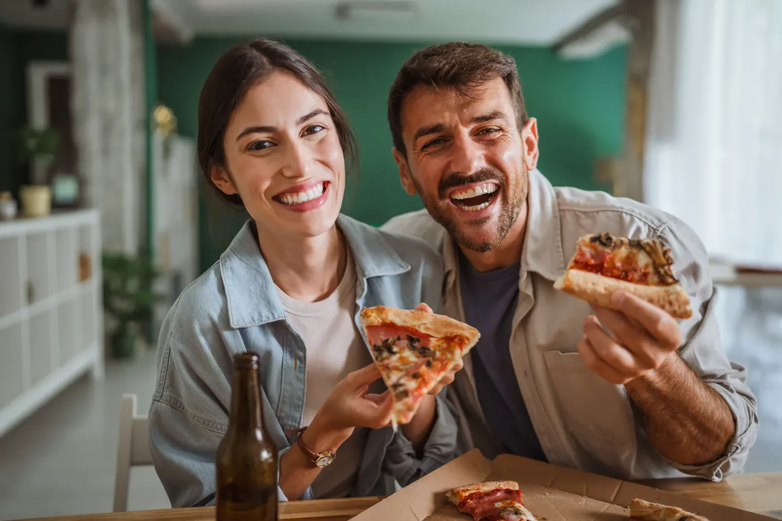 Happy couple enjoying pizza together at home, a meal that comes up in the cheat day question