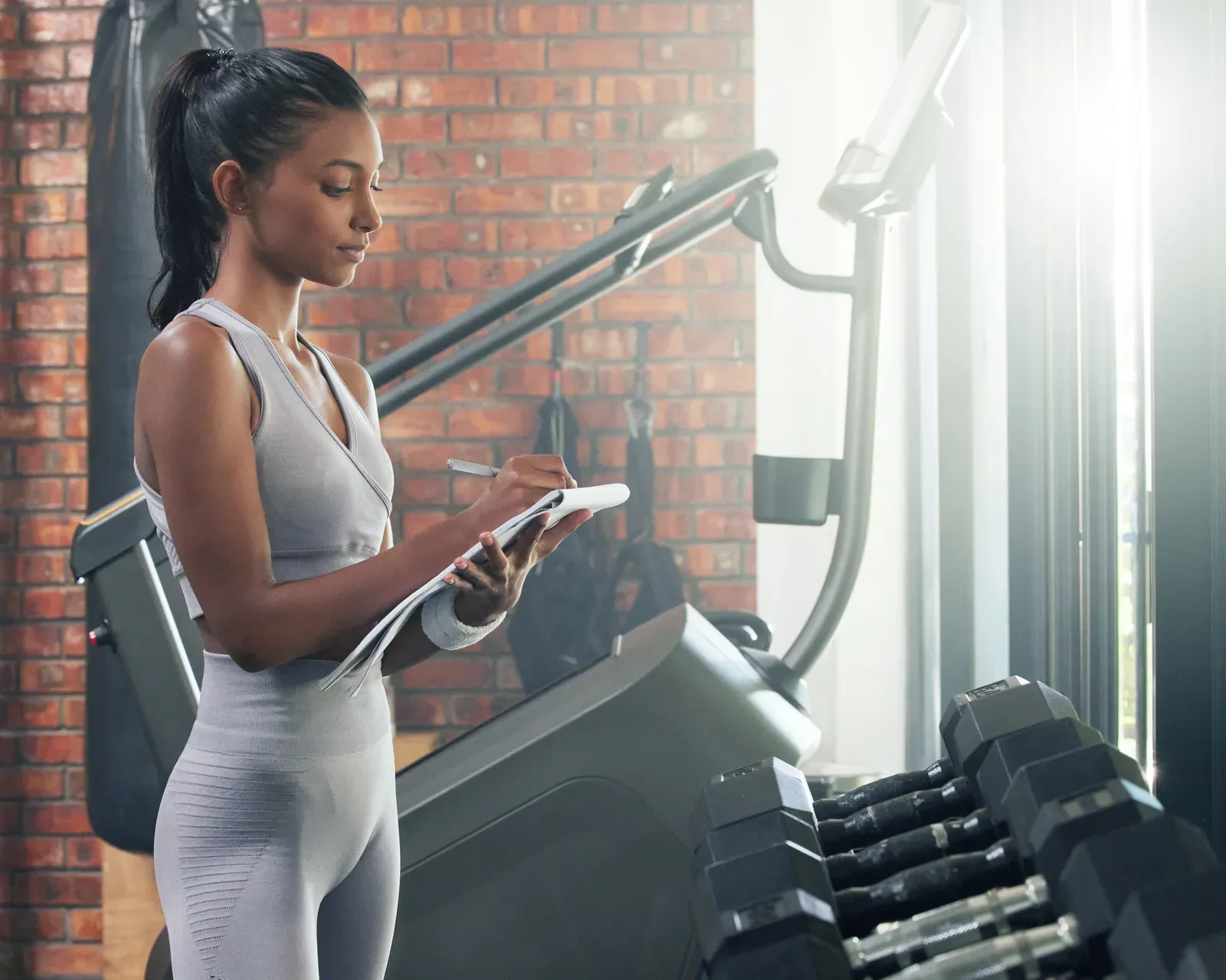 Young woman writing notes in a gym, tracking weights and reps for double progression