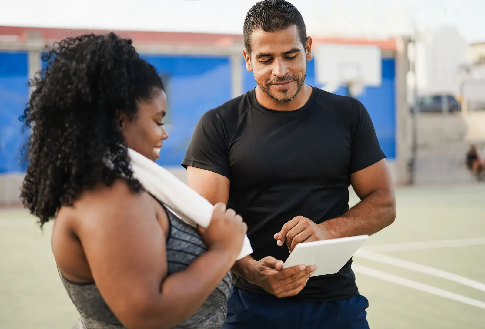 Larger-bodied woman talking with her personal trainer outdoors while checking a clipboard, a supportive first conversation