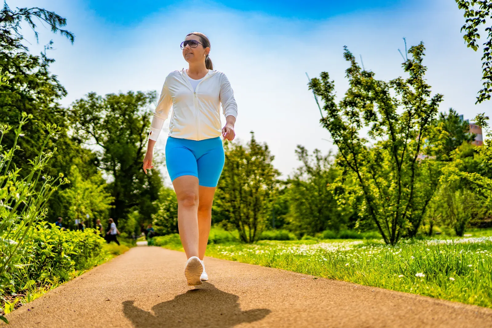 Middle aged woman walking in a city park on a summer day, a gentle way to restart exercise after loss