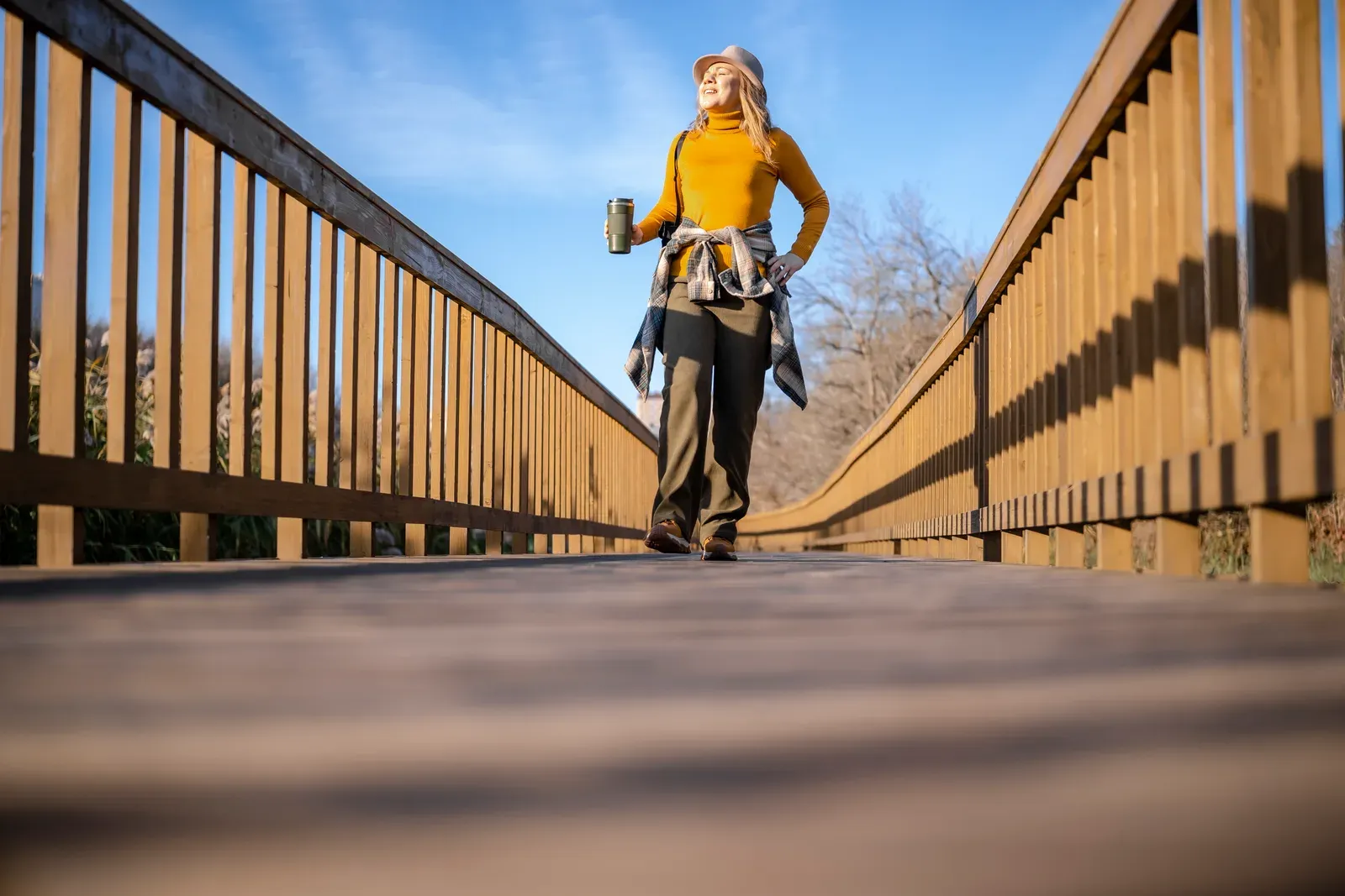 Woman walking alone on a wooden boardwalk in an autumn park near a lake, an easy return to movement after pneumonia