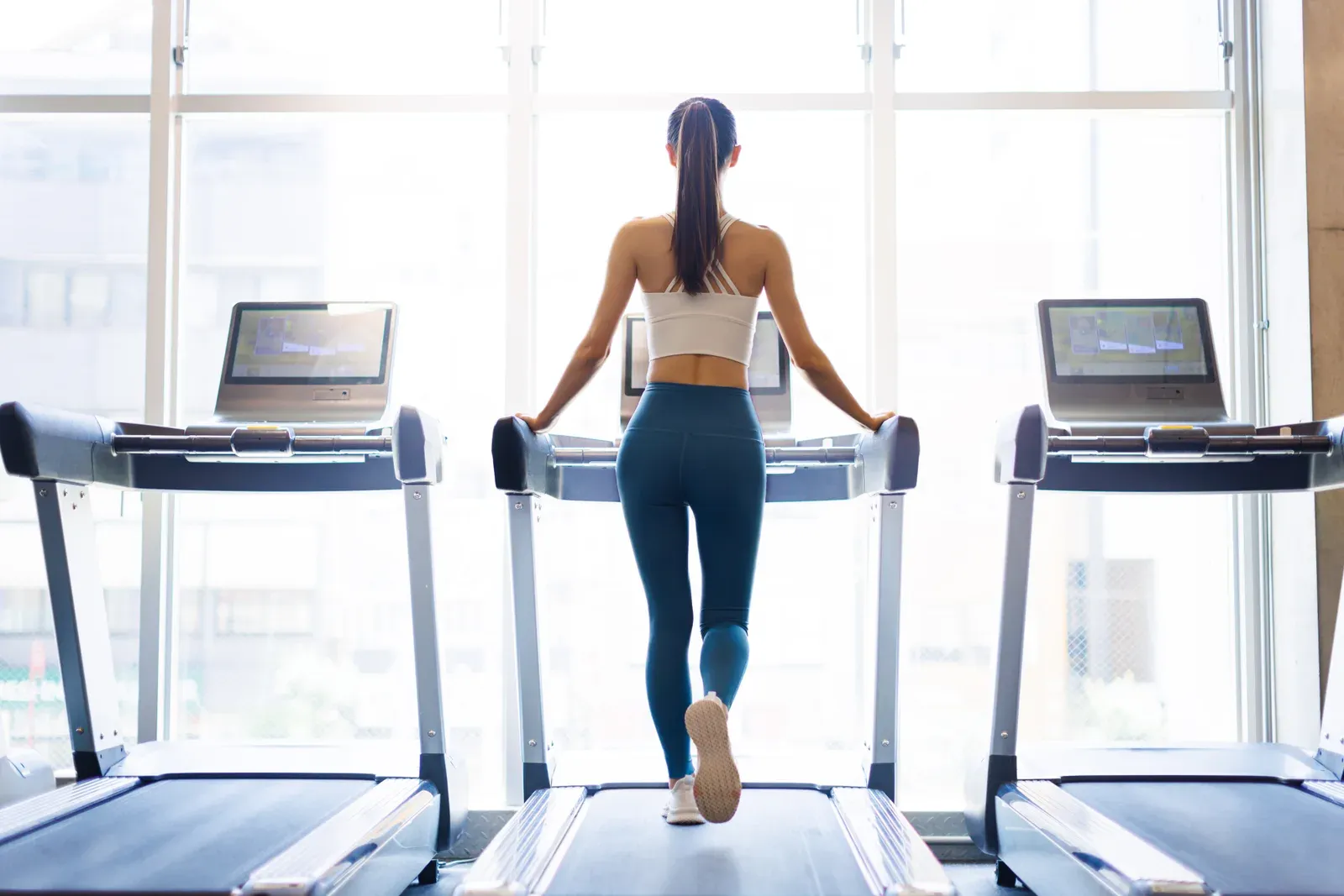 Rear view of a young woman walking on a treadmill, a low-intensity option during treatment