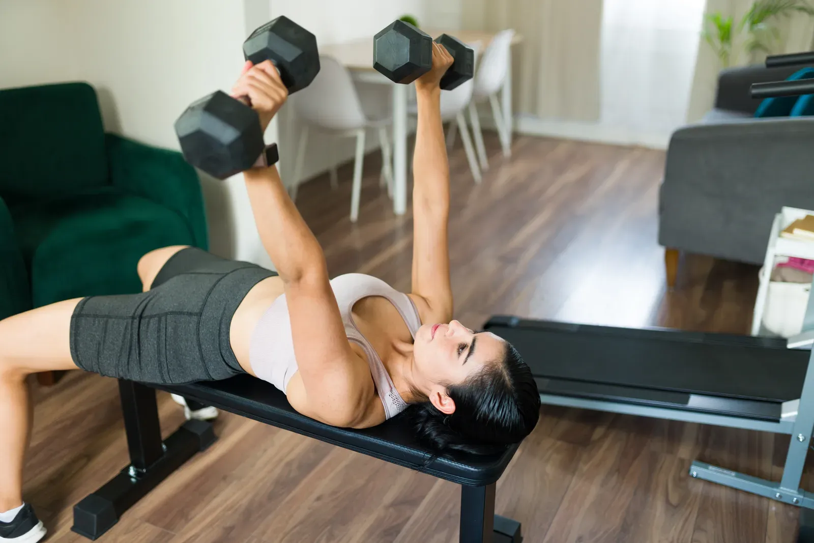 Woman lifting weights on a workout bench in her living room, home strength training to support weight loss