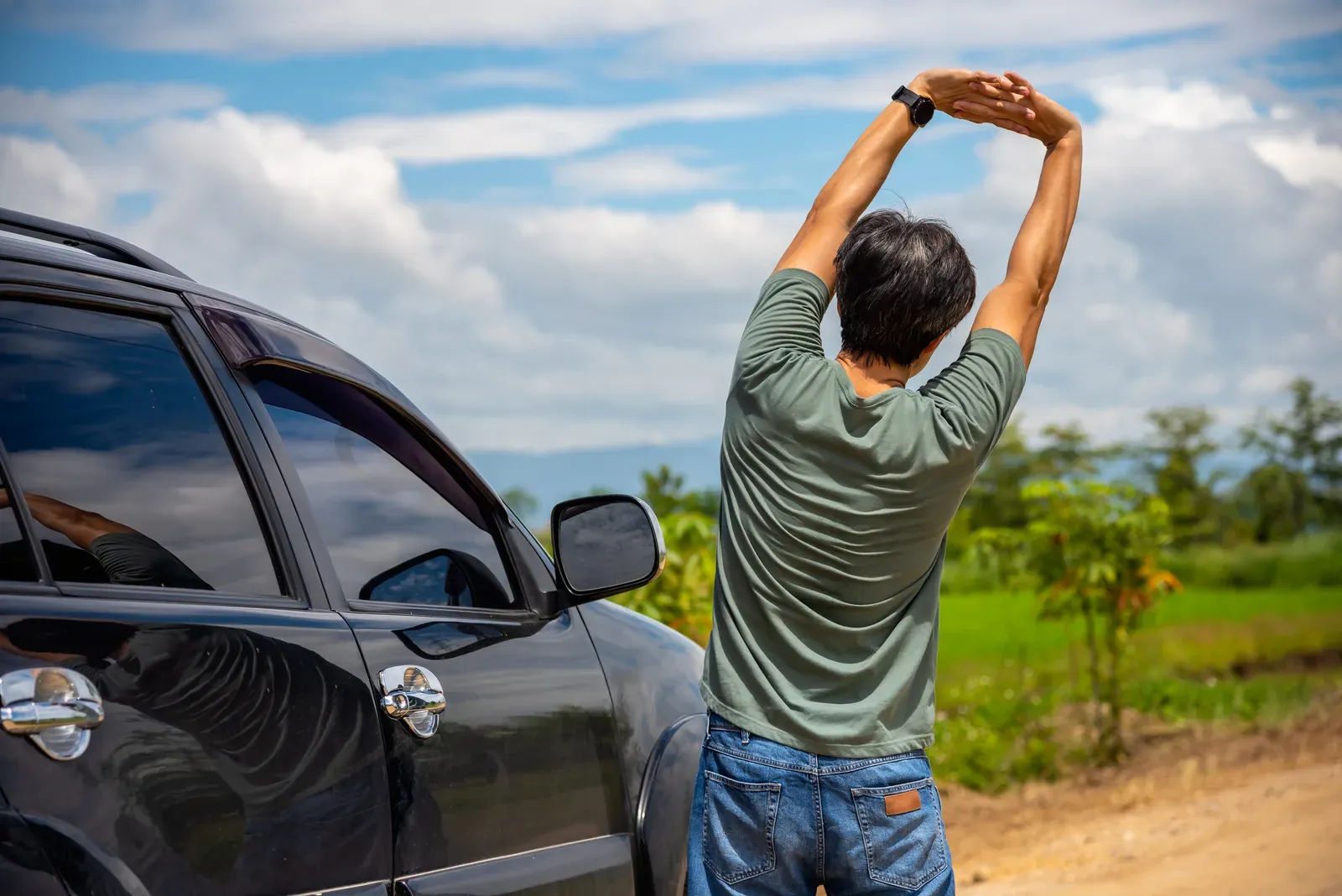 Man stretching beside his car after a long drive to relieve back pain, a break for people who sit all day