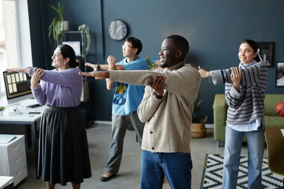 Colleagues doing standing arm stretches together in an office