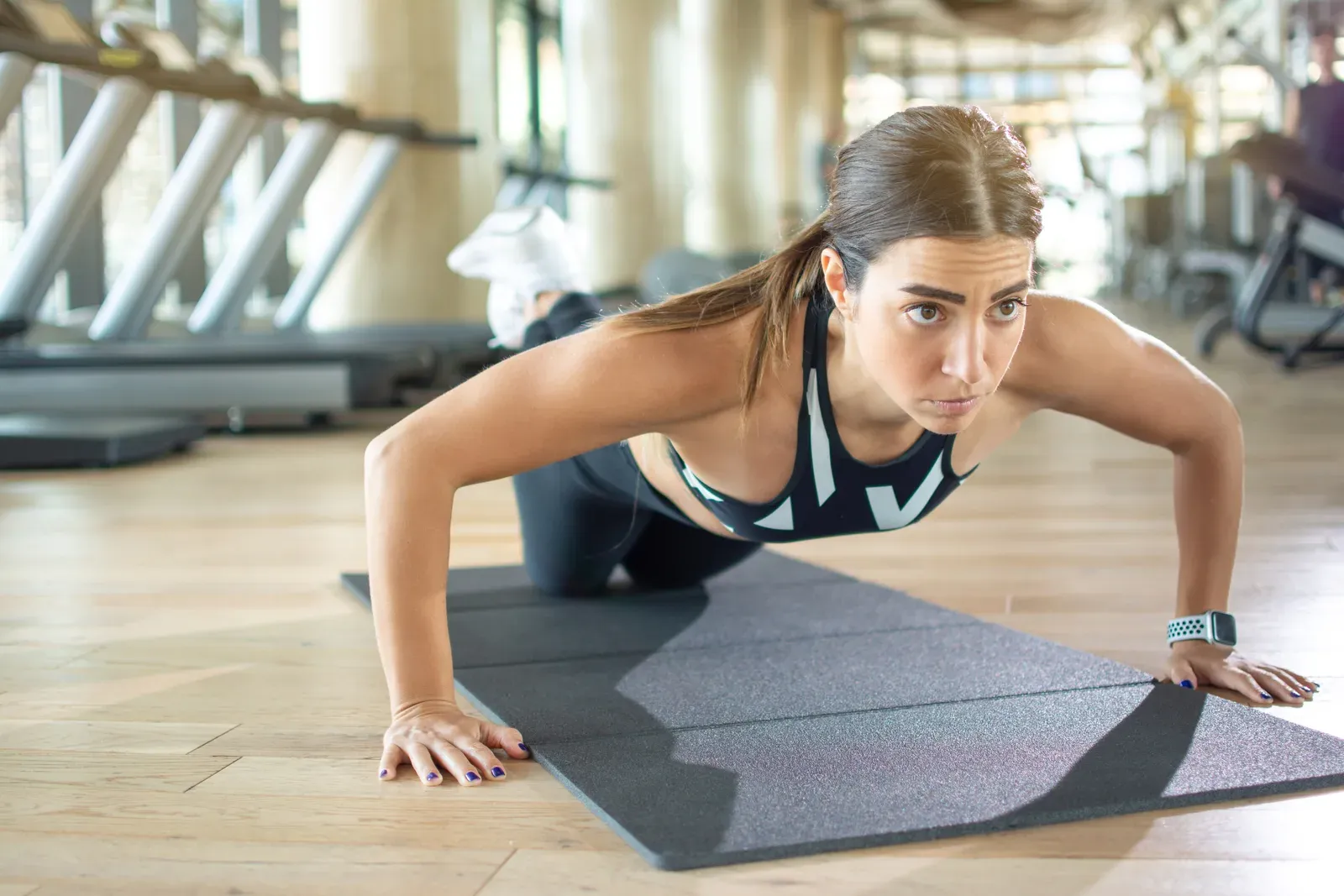 Young woman doing knee push-ups on an exercise mat at the gym, a scaled version of a classic upper body move