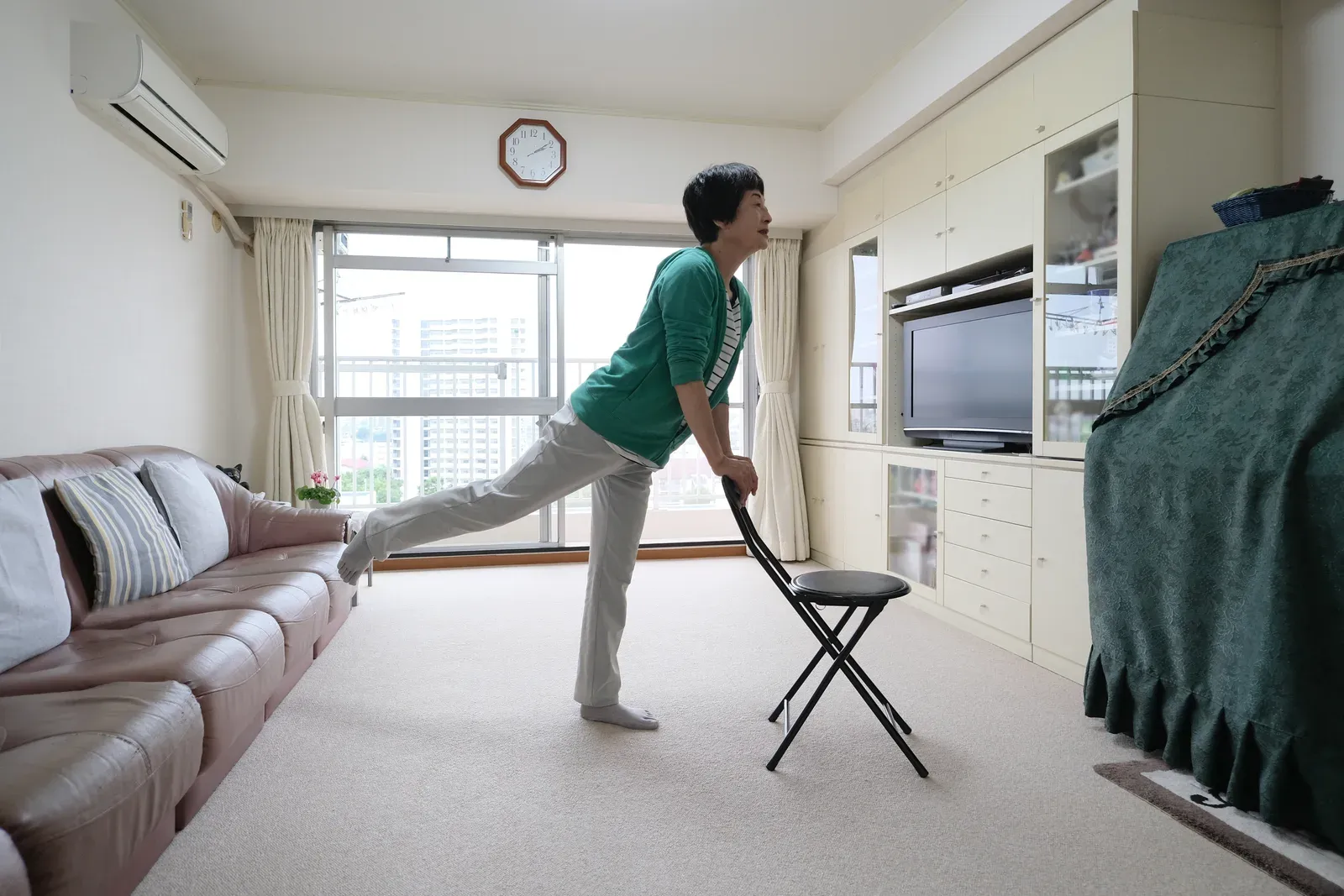 An older woman doing a standing exercise with a chair for support at home