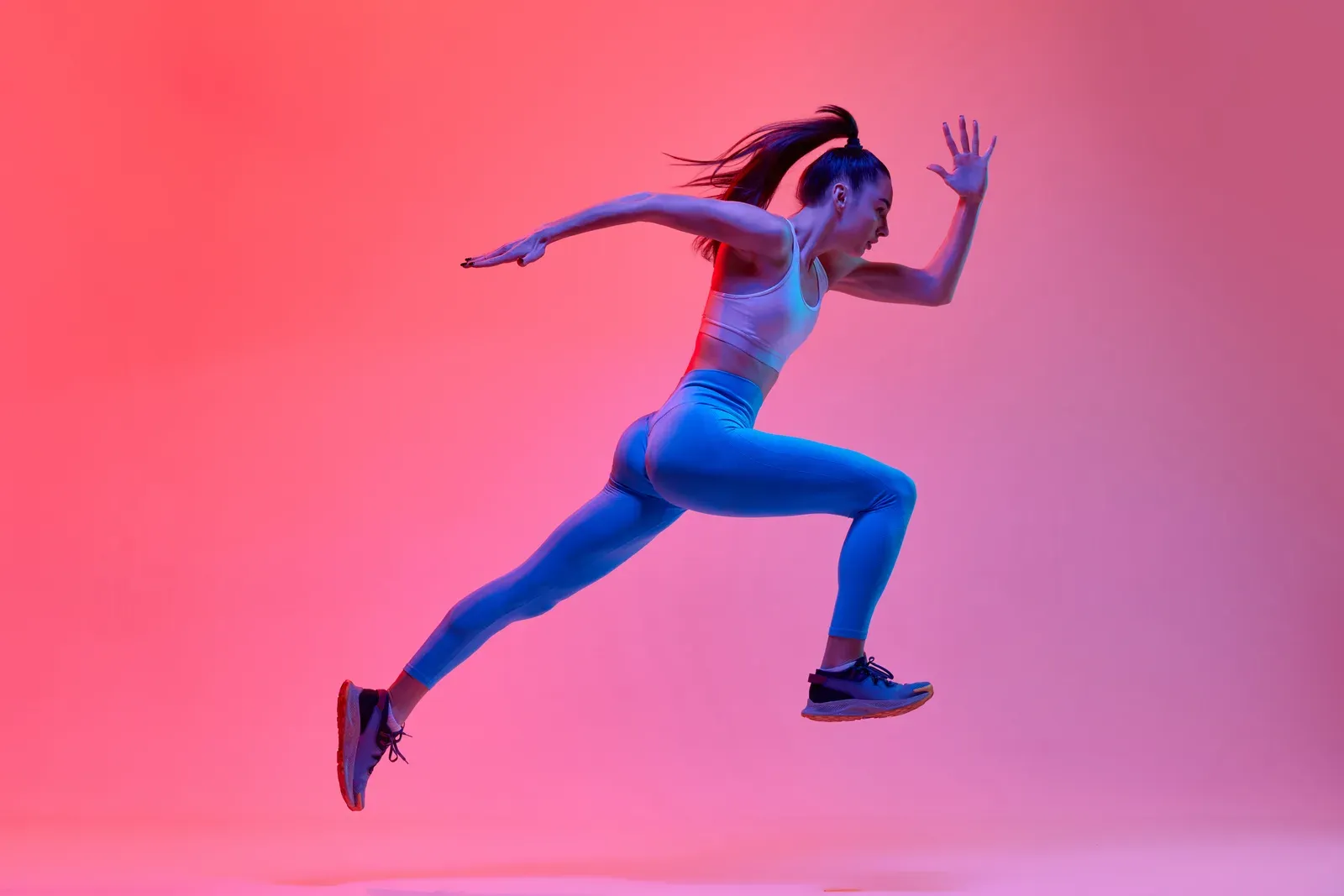 Young active woman runner in motion against a pink neon studio background, staying active while trying to conceive