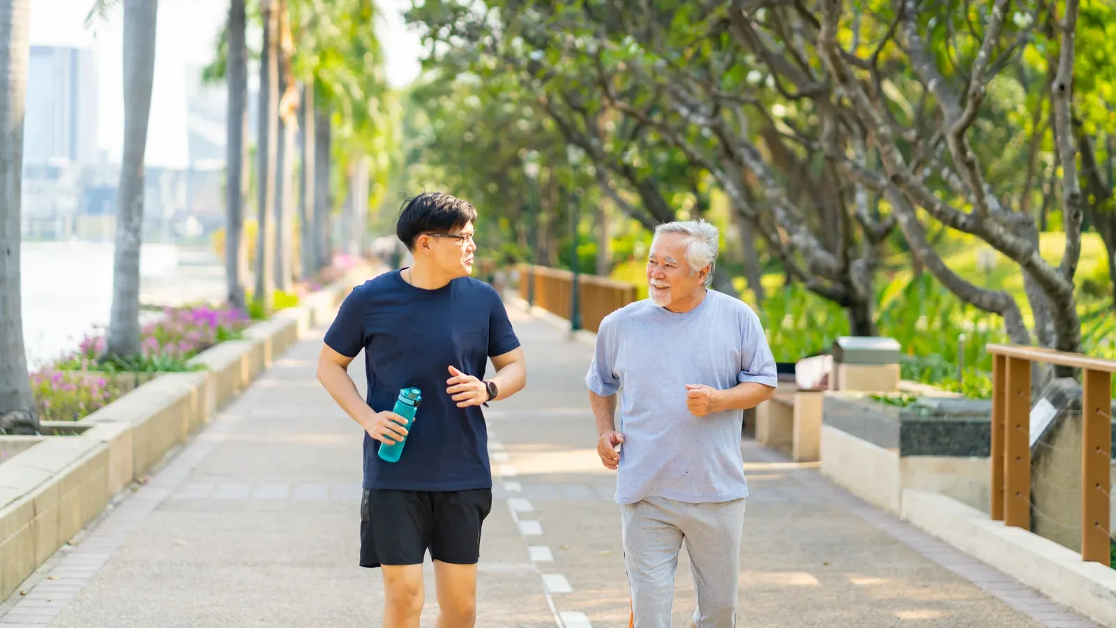 Asian adult son and elderly father jogging together in a park, shared exercise with an aging parent