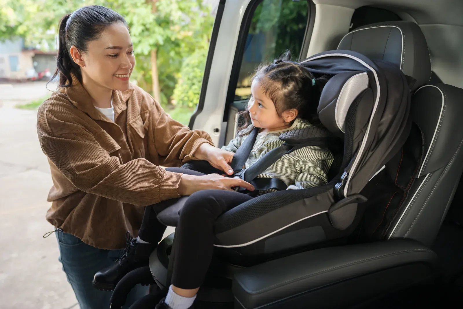 Mother fastening a preschool child into a car seat, a daily lift that strength training can make easier