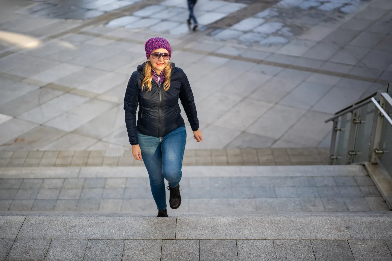 Middle-aged woman walking up concrete stairs in the city, an everyday task that strength work can ease