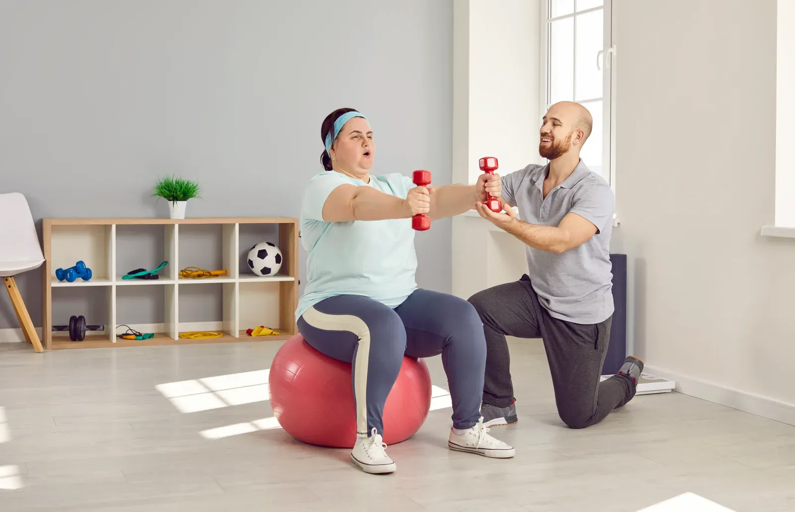 Larger-bodied woman training with dumbbells under the guidance of a personal trainer in a gym
