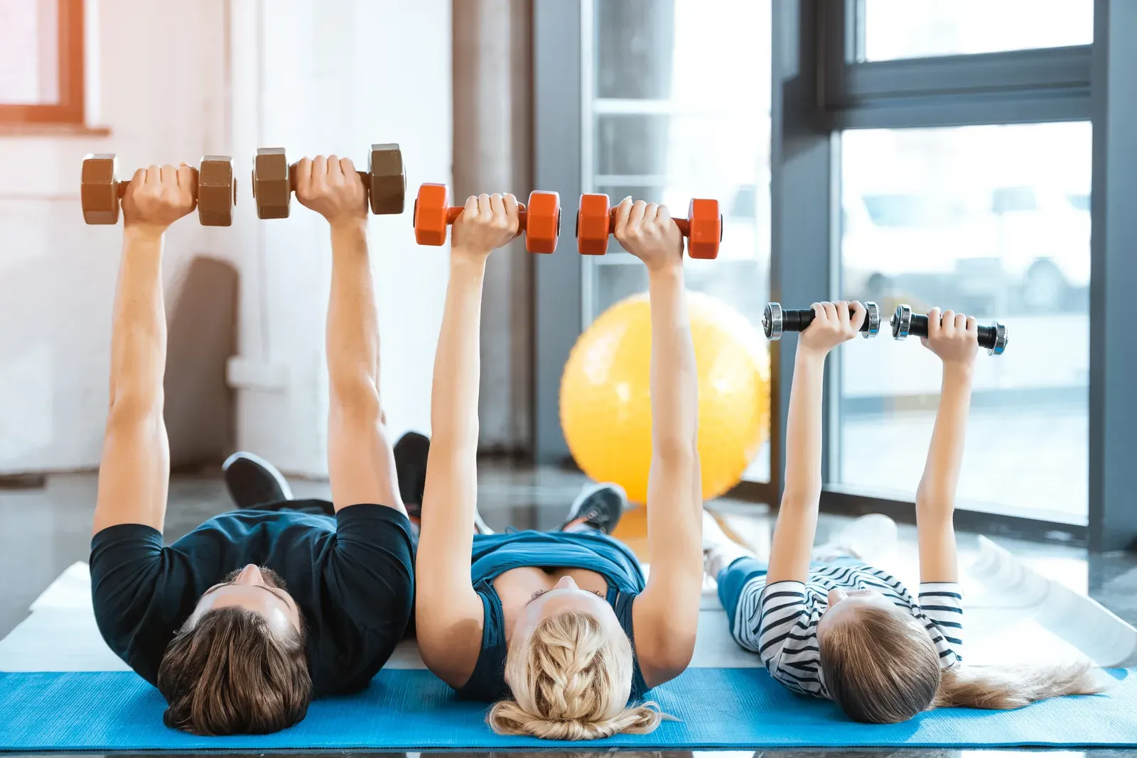 Happy family exercising with dumbbells at a fitness studio, a shared activity behind family memberships