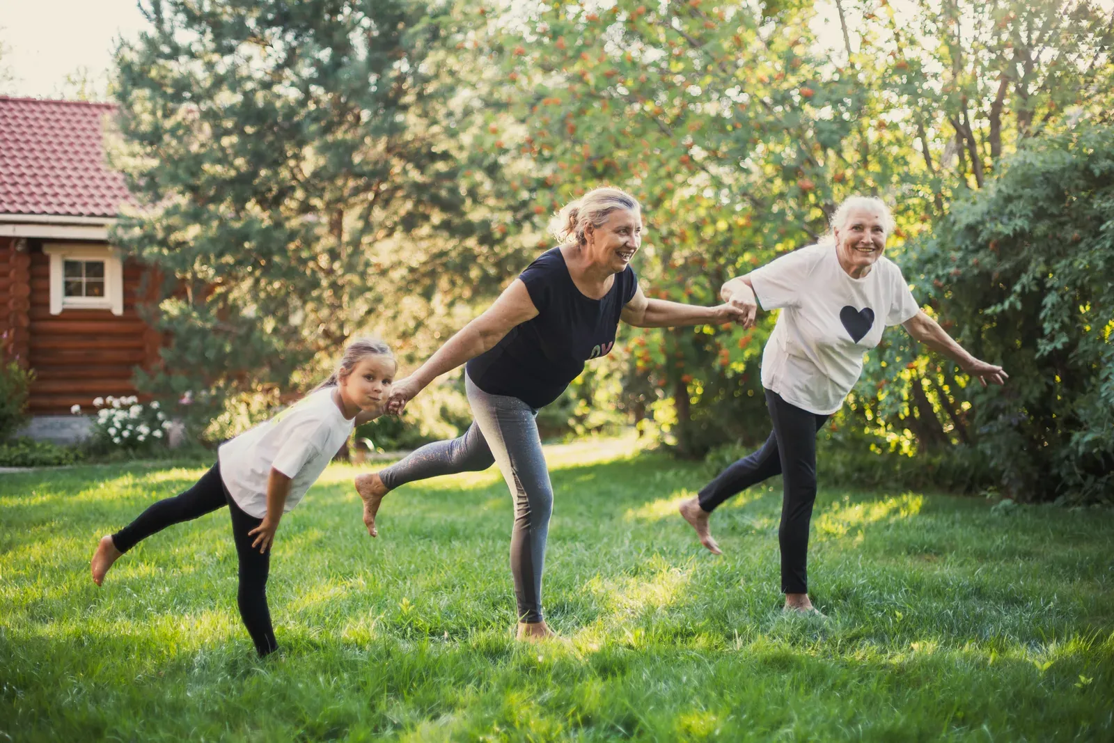 Three generations of women smiling and balancing on one leg while holding hands, family exercise together