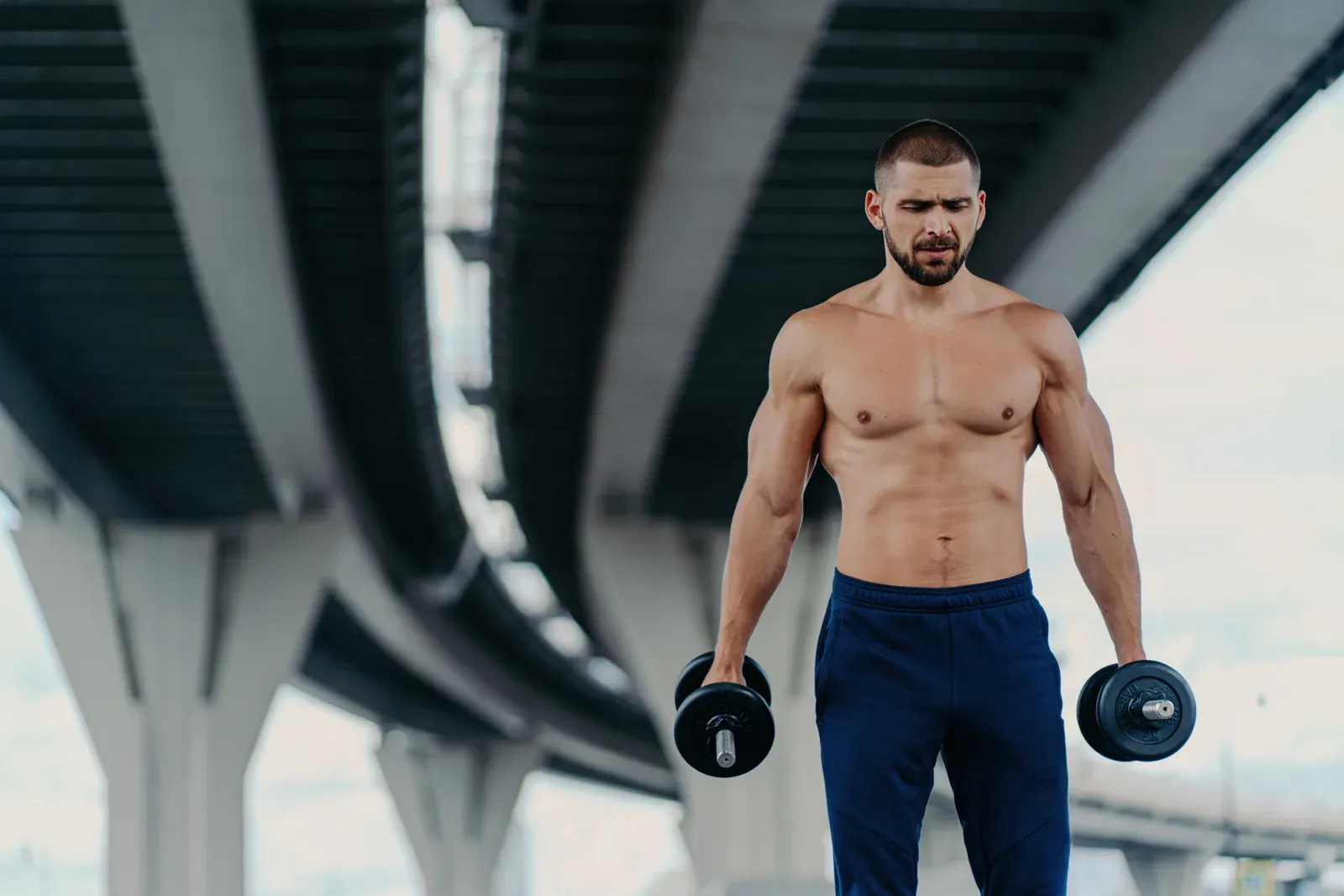 Serious bearded man preparing for a barbell workout outdoors, showing the grip and arm strength carries build