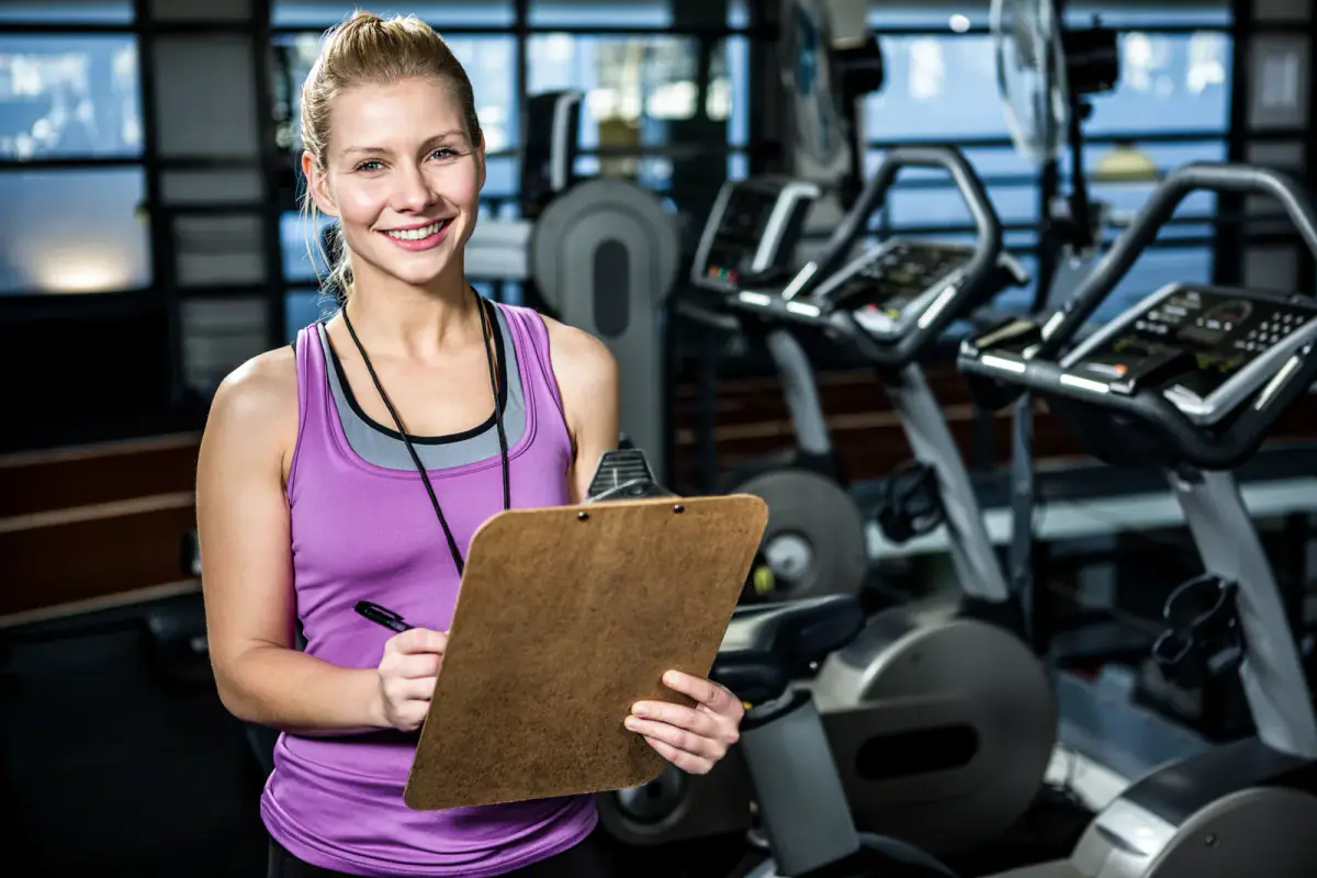 A trainer recording baseline fitness measurements on a clipboard beside a client