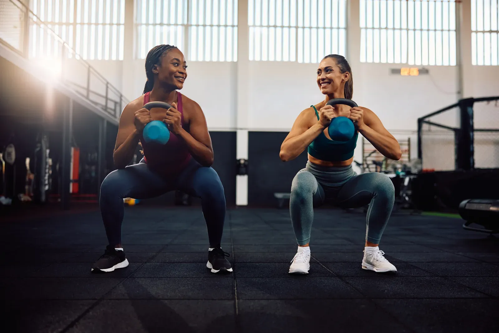 Happy athletic women exercising with kettlebells during a gym workout, a habit to start in your 20s