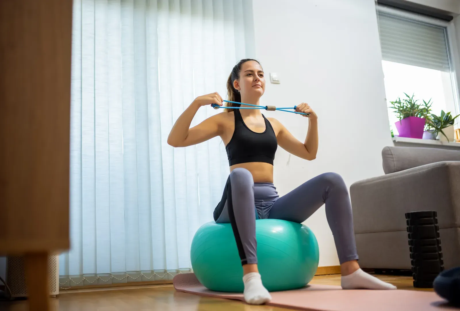Female athlete doing resistance band face pulls on a Pilates ball, a strength move for rounded shoulders
