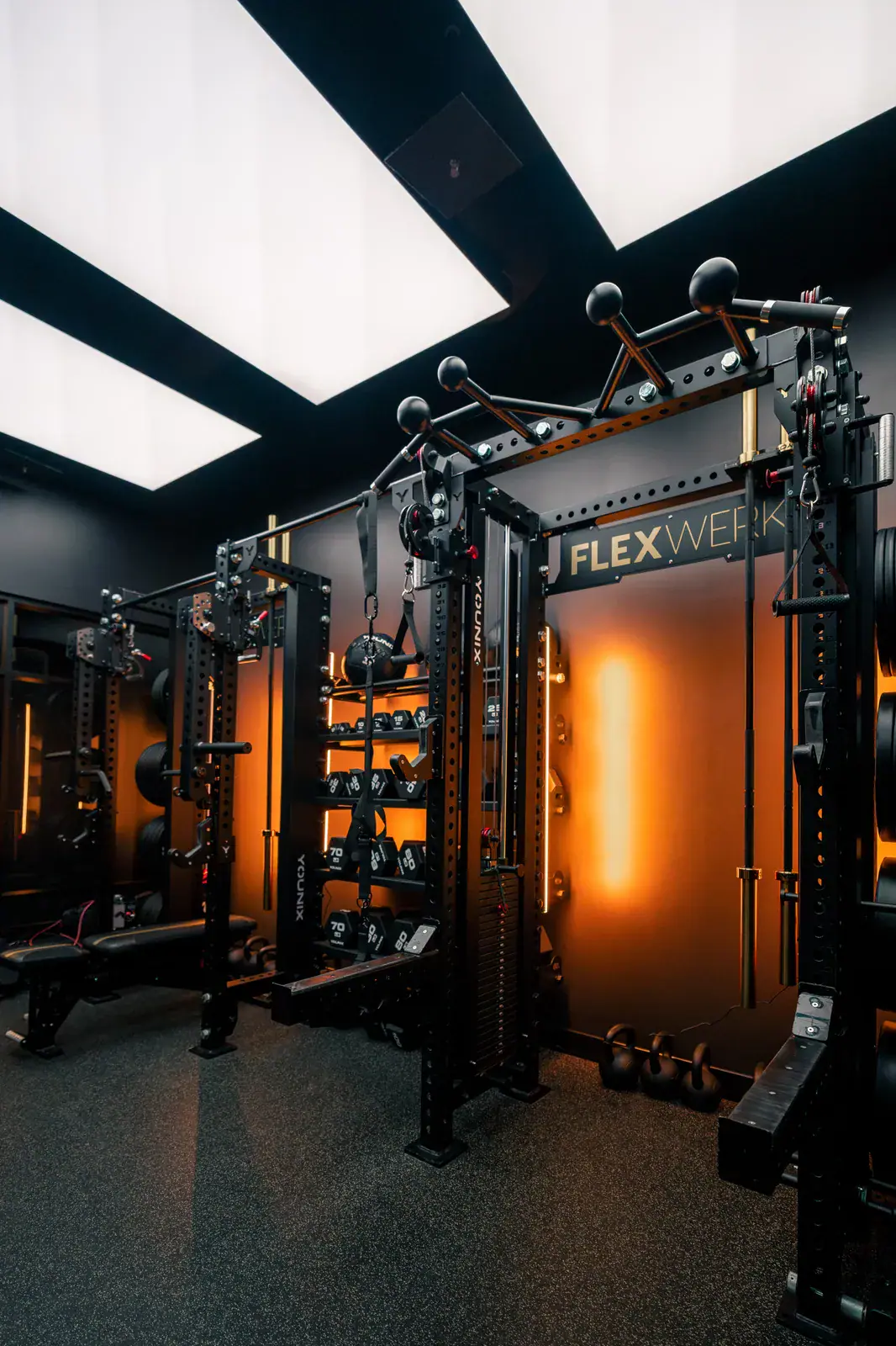 Amber-lit racks, cable stations, and barbells lining a FlexSpace Plus training room at FlexWerk Carmel
