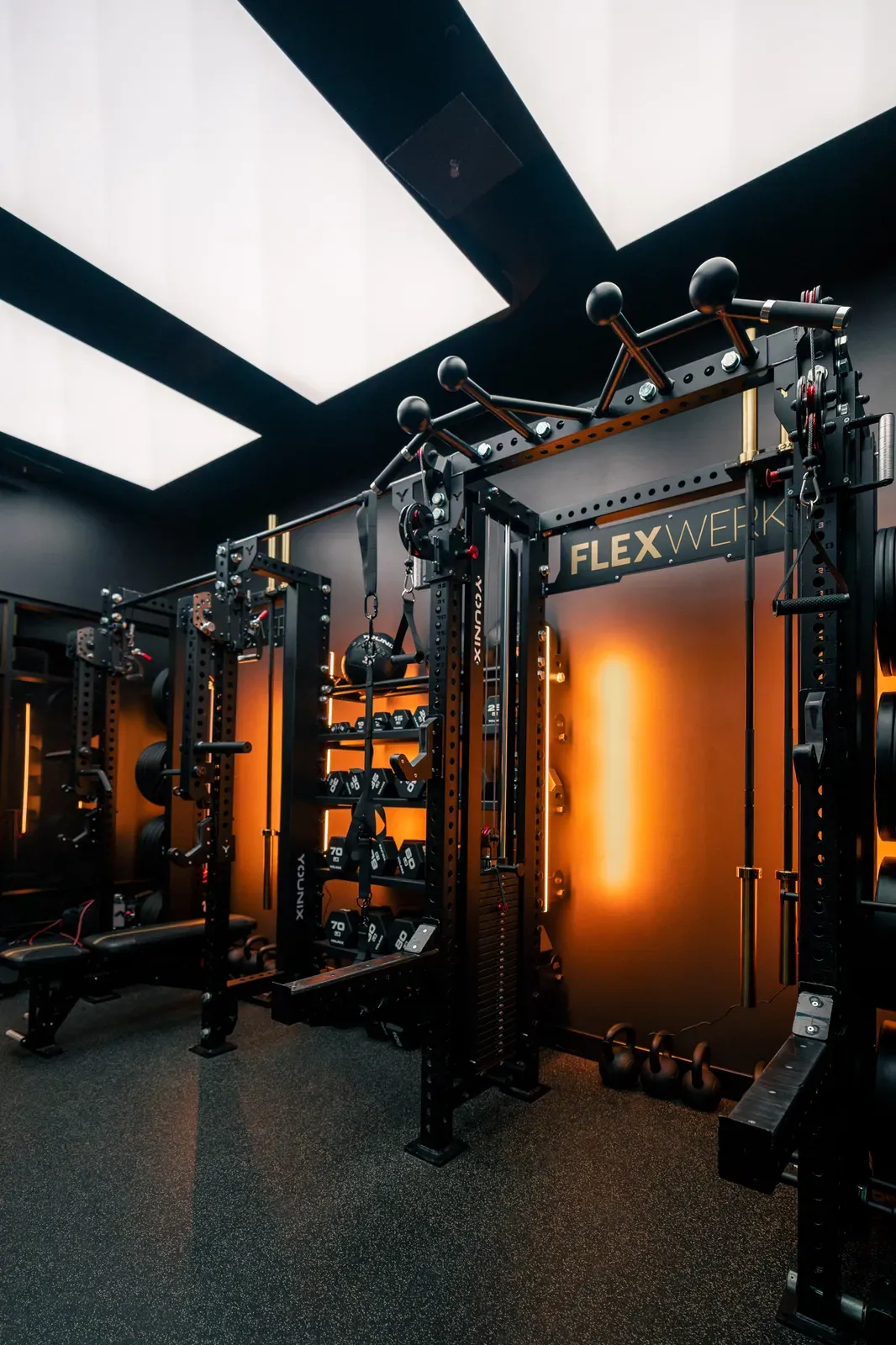 Amber-lit racks, cable stations, and barbells lining a FlexSpace Plus training room at FlexWerk Carmel