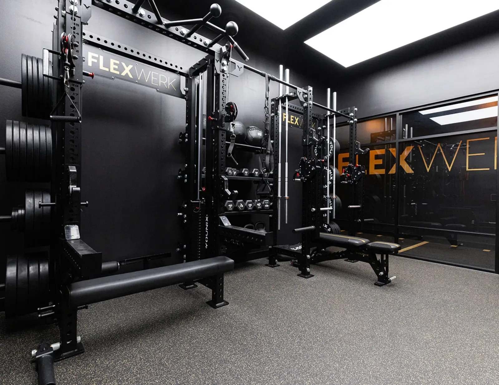 Dual racks with lever arms, barbells, and bumper plates inside a FlexSpace Plus at FlexWerk Carmel