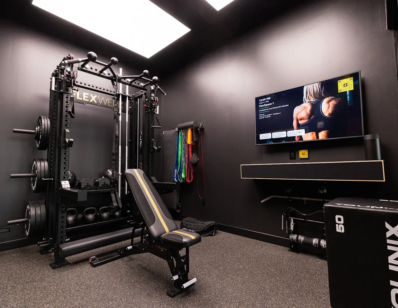 Inside a FlexSpace Standard private gym room at FlexWerk Carmel with a functional rack, adjustable bench, and personal TV